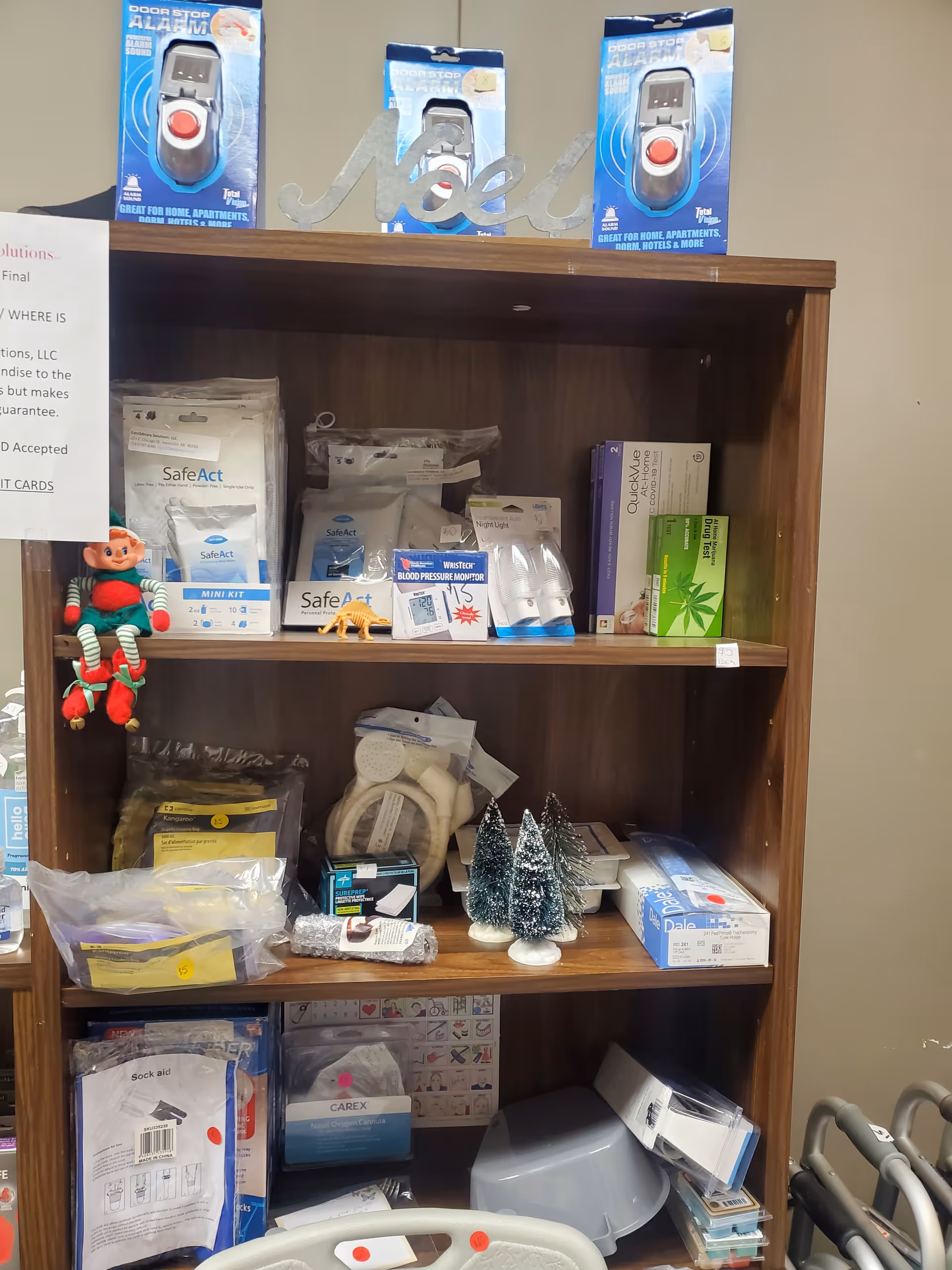 Wooden shelf stocked with medical supplies and devices, plus small Christmas trees and a hanging elf.