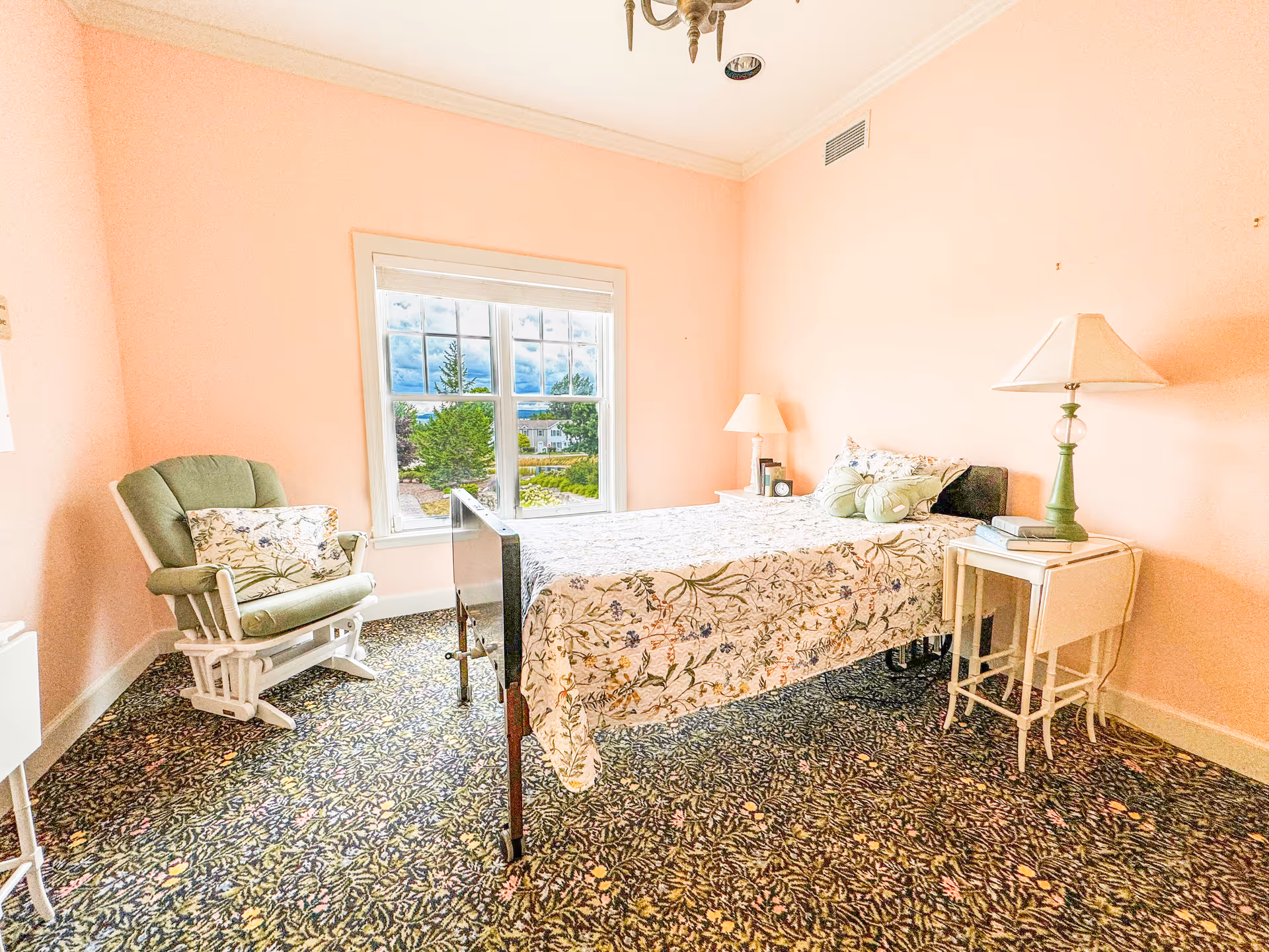 Pink bedroom with floral bedspread, green chair, and window view.