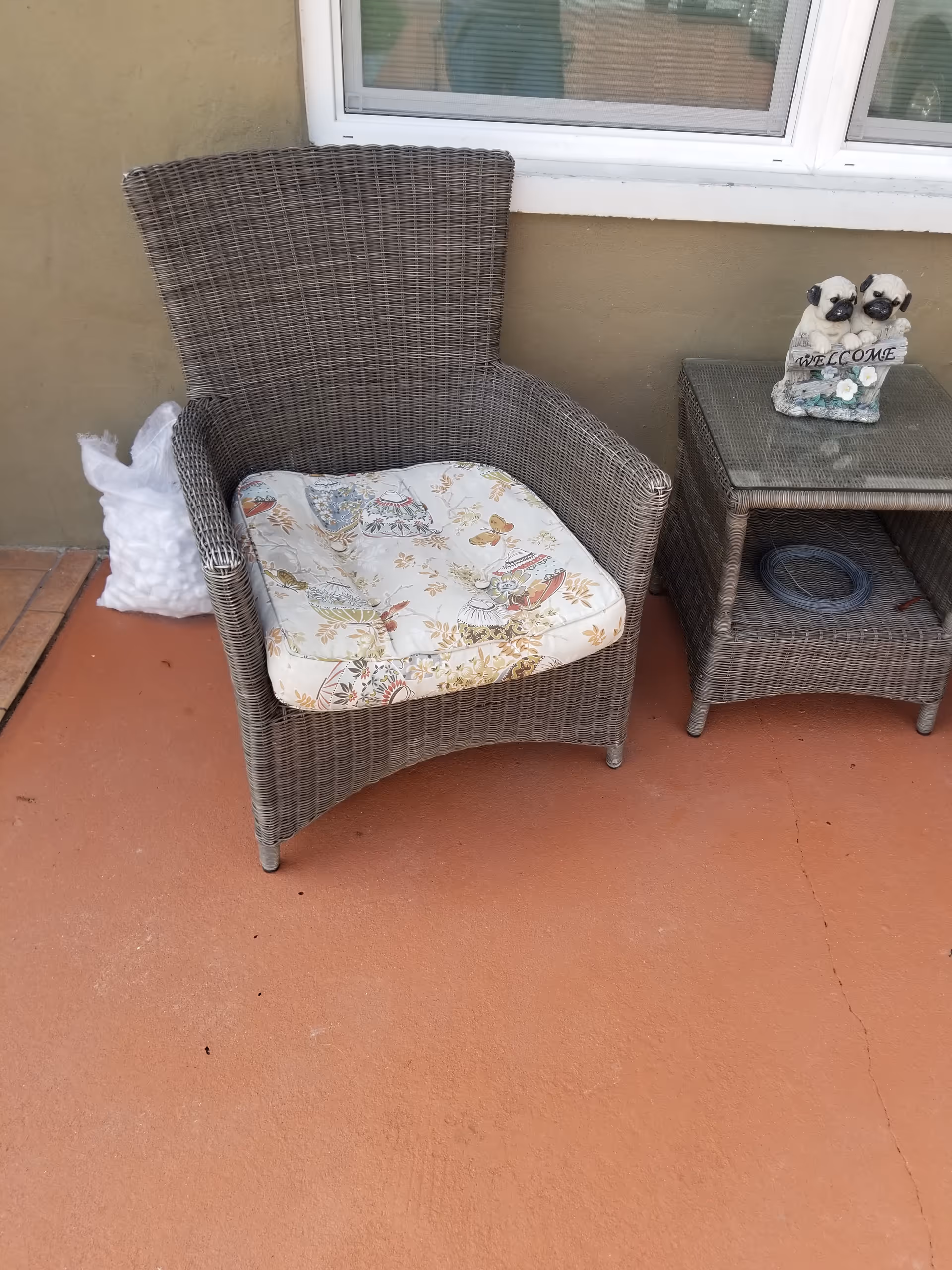 Wicker outdoor chair with floral cushion beside a small table on a sunny patio.