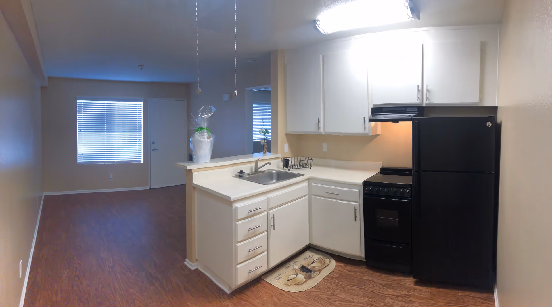 Bright kitchen with white cabinets, sink, stove, and a black refrigerator in a senior living unit.