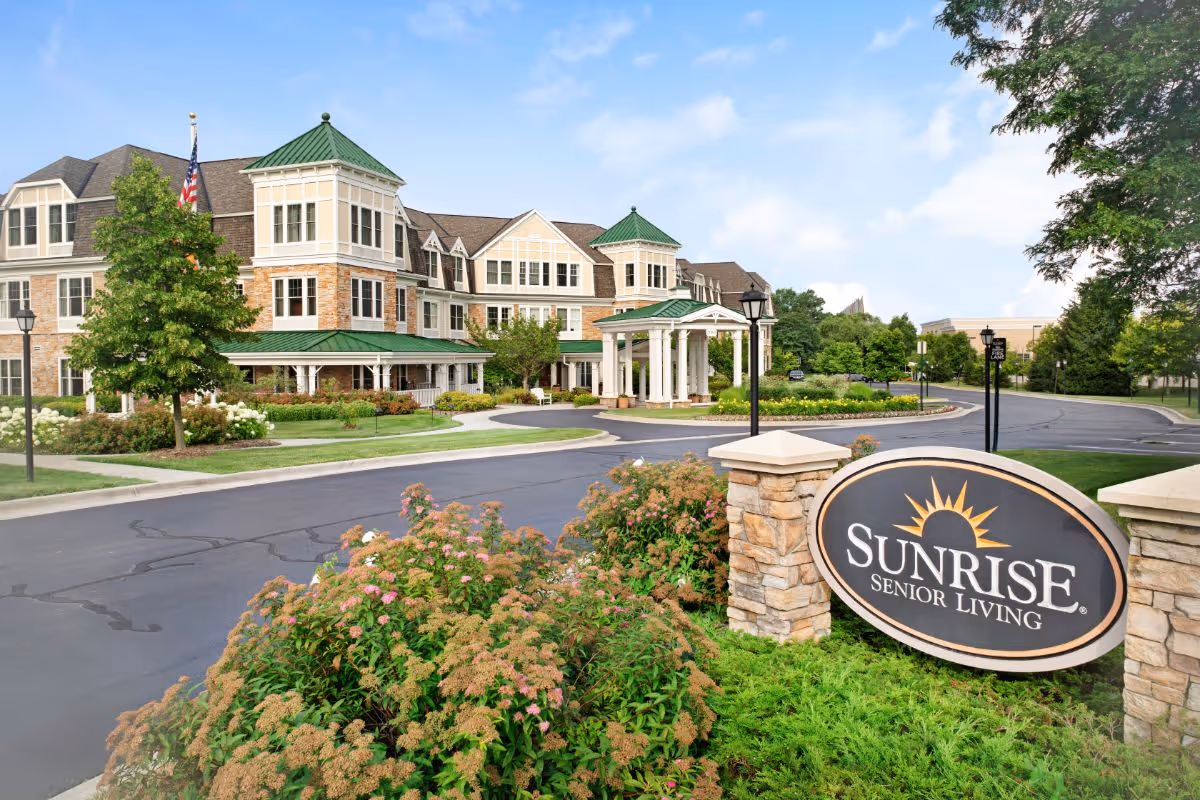 Front exterior of Sunrise Senior Living with landscaped entrance, circular driveway, and facility sign.