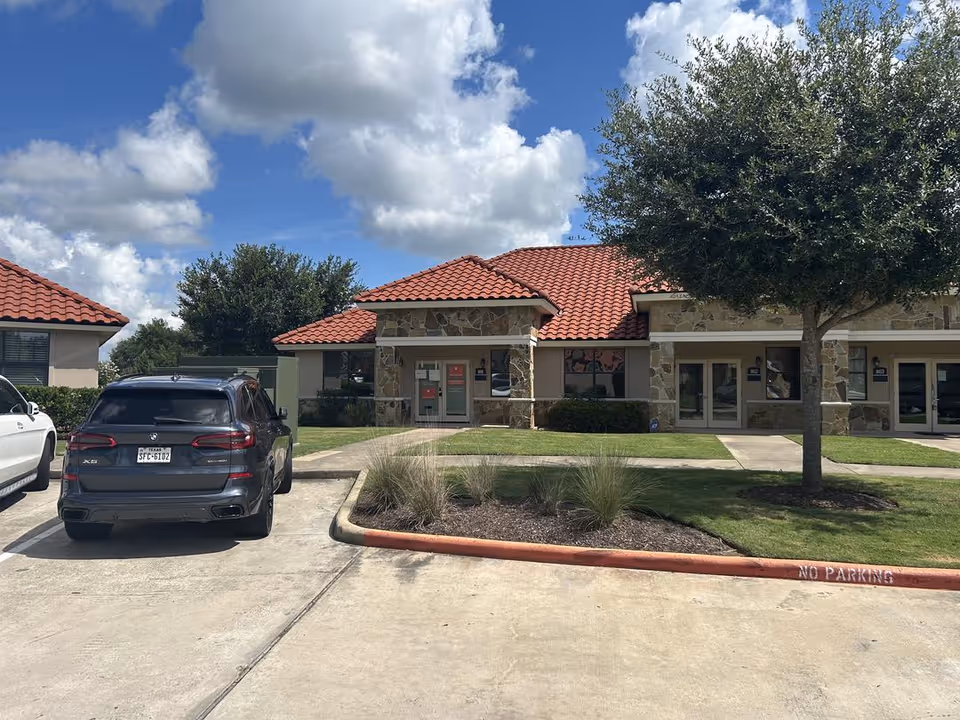 Exterior view of a senior care facility with red-tiled roof and parked cars.