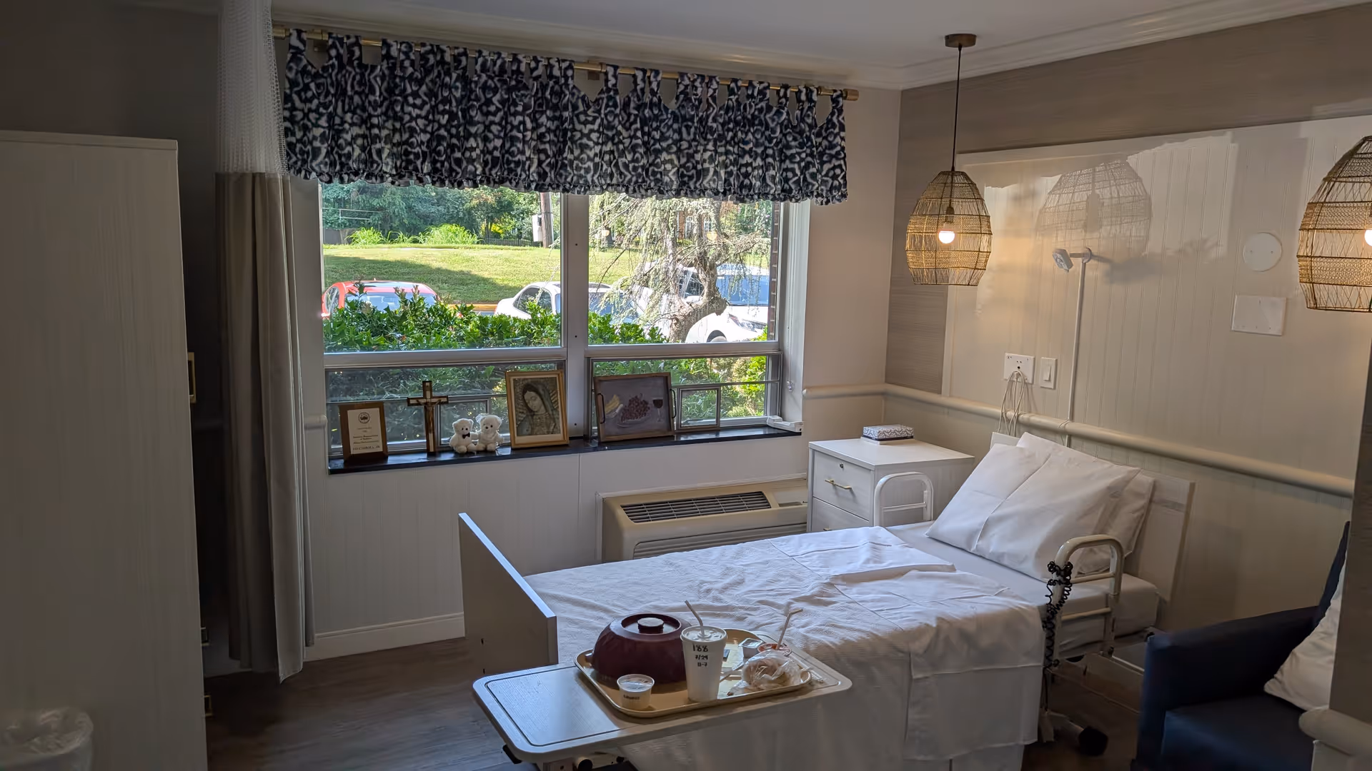 Bright senior living bedroom with a white bed, nightstand, window, and framed photos on the sill
