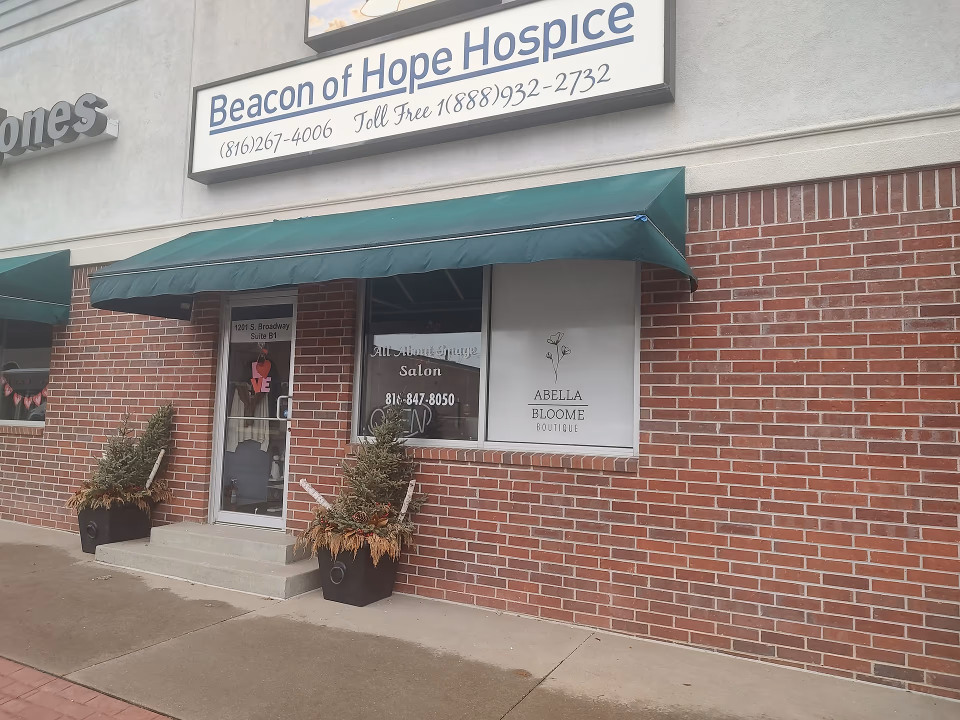 Brick storefront with Beacon of Hope Hospice sign, green awning, and potted plants.