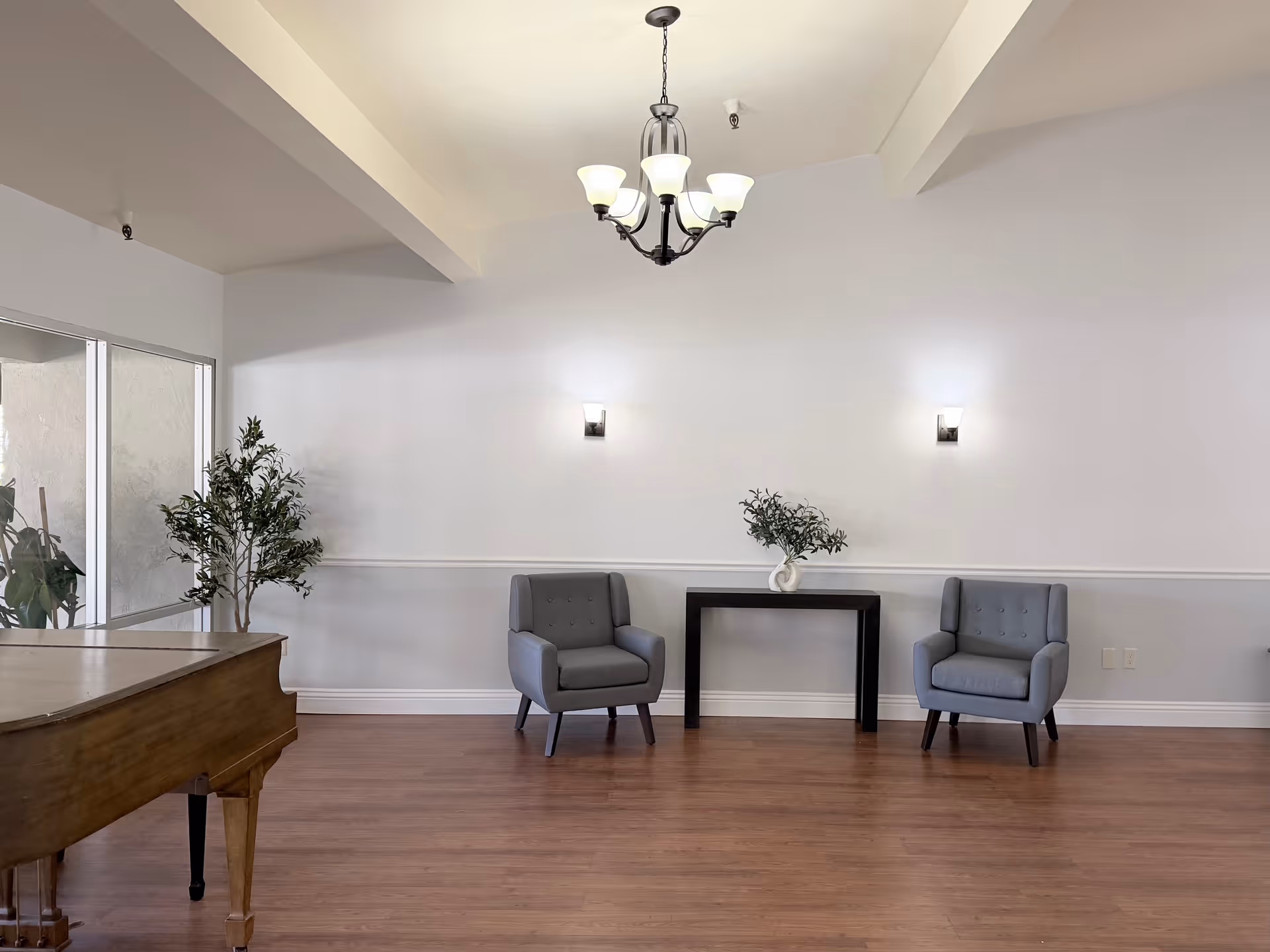 A bright lobby area with two gray chairs, a piano, plants, and a console table.