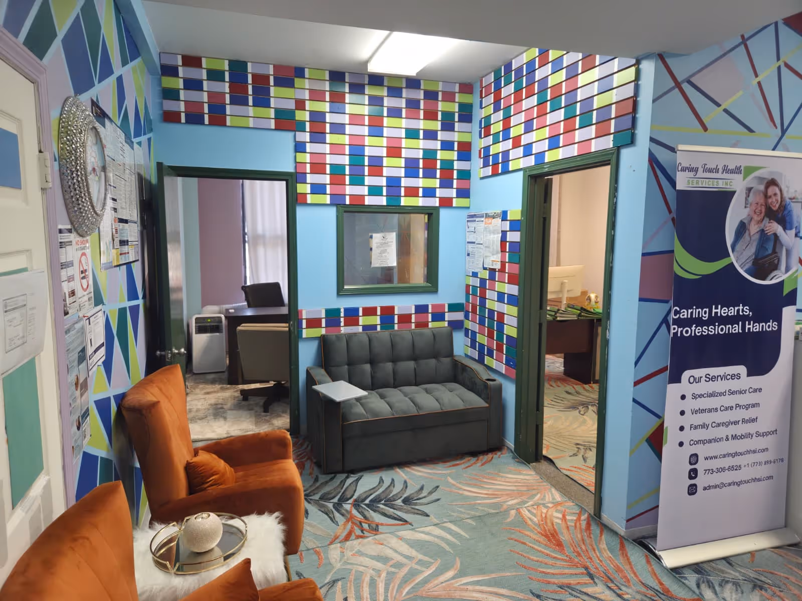 Colorful geometric walls surround a small waiting area with a gray couch and orange chairs.