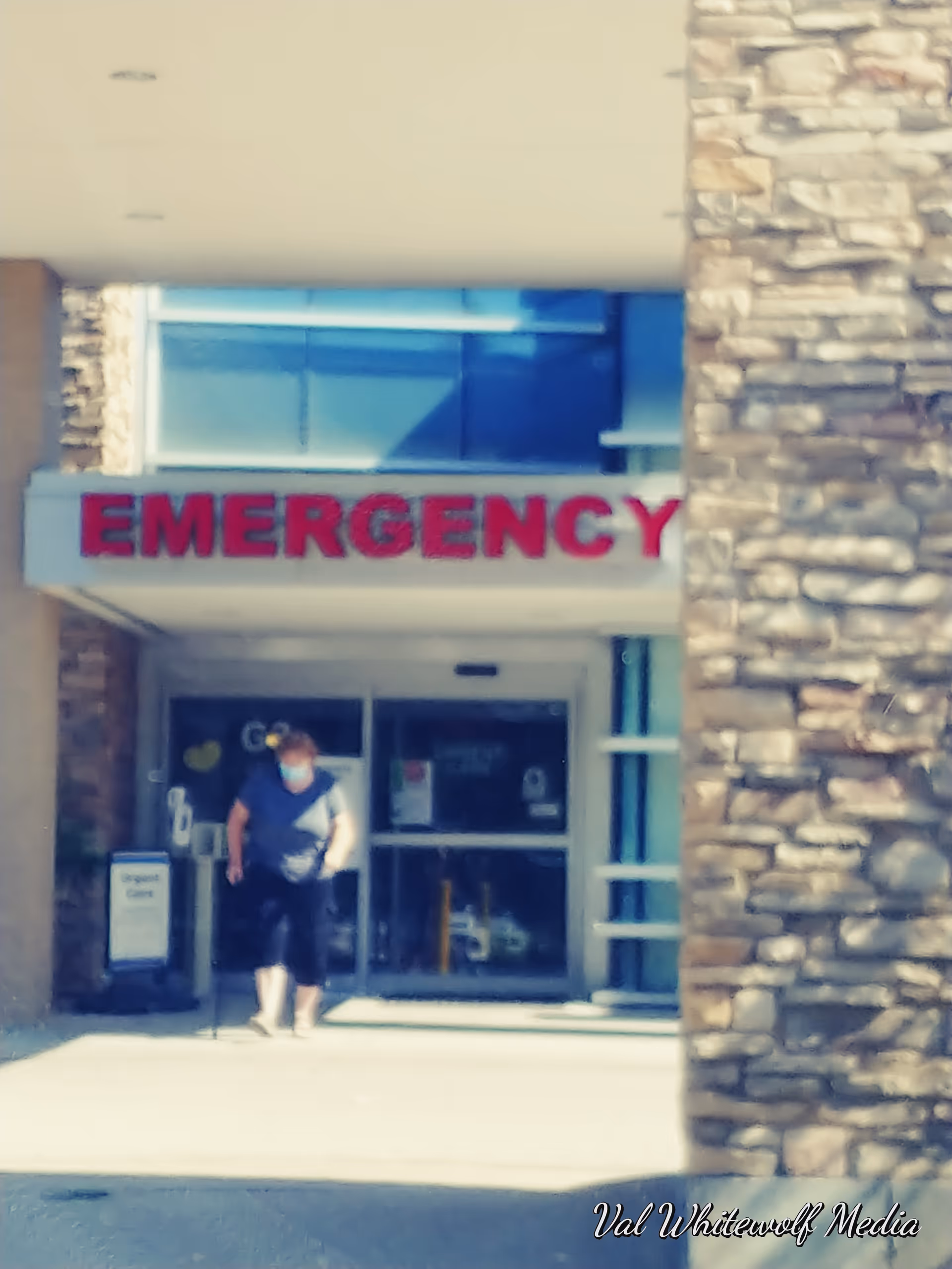 Person wearing a mask exits a facility under an EMERGENCY entrance sign.