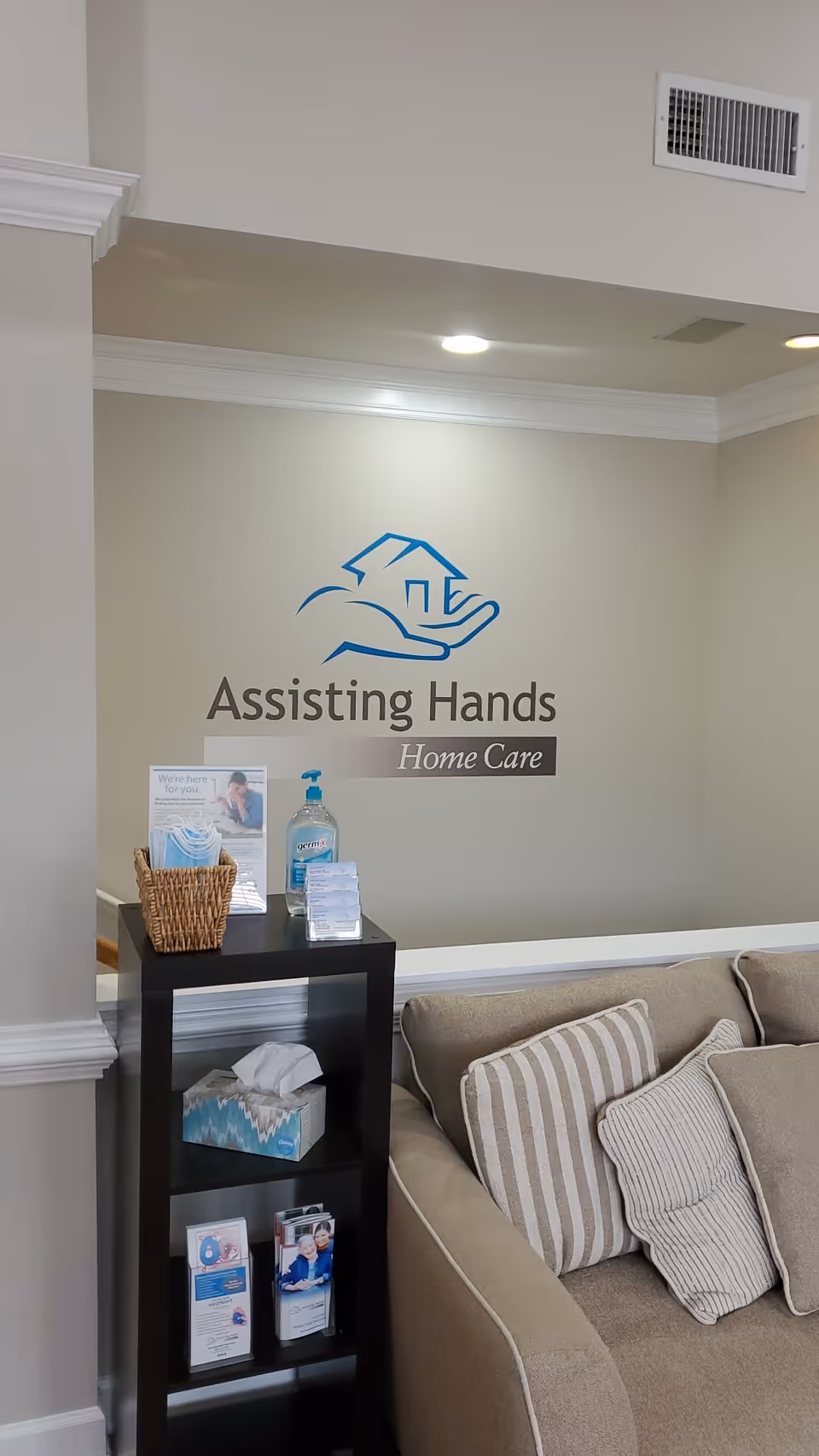 Reception area featuring Assisting Hands Home Care logo and a beige sofa.