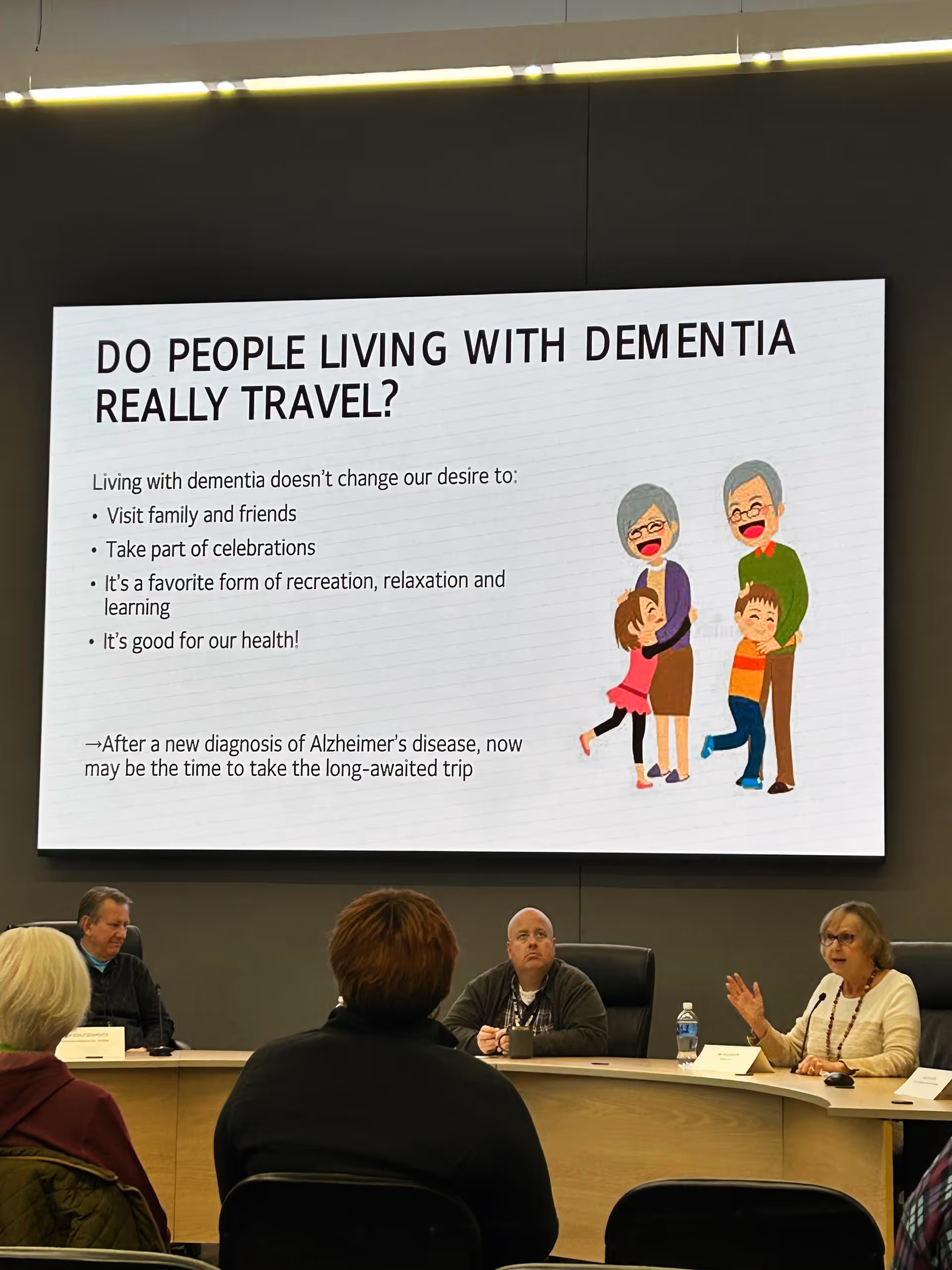 Panel and audience in a conference room with a large dementia presentation on screen.
