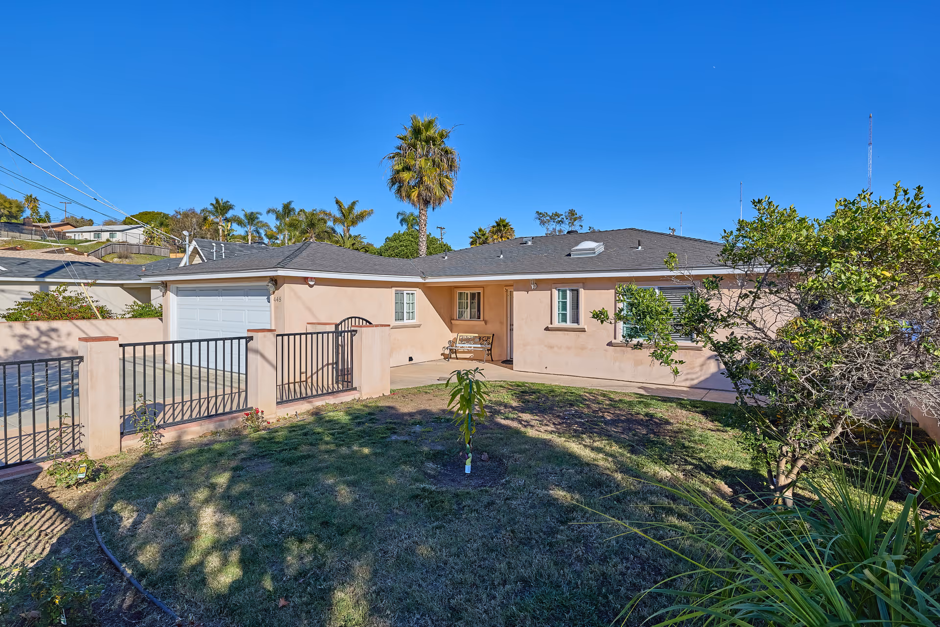 Single-story peach care home with a fenced yard, palm trees, and clear blue sky.