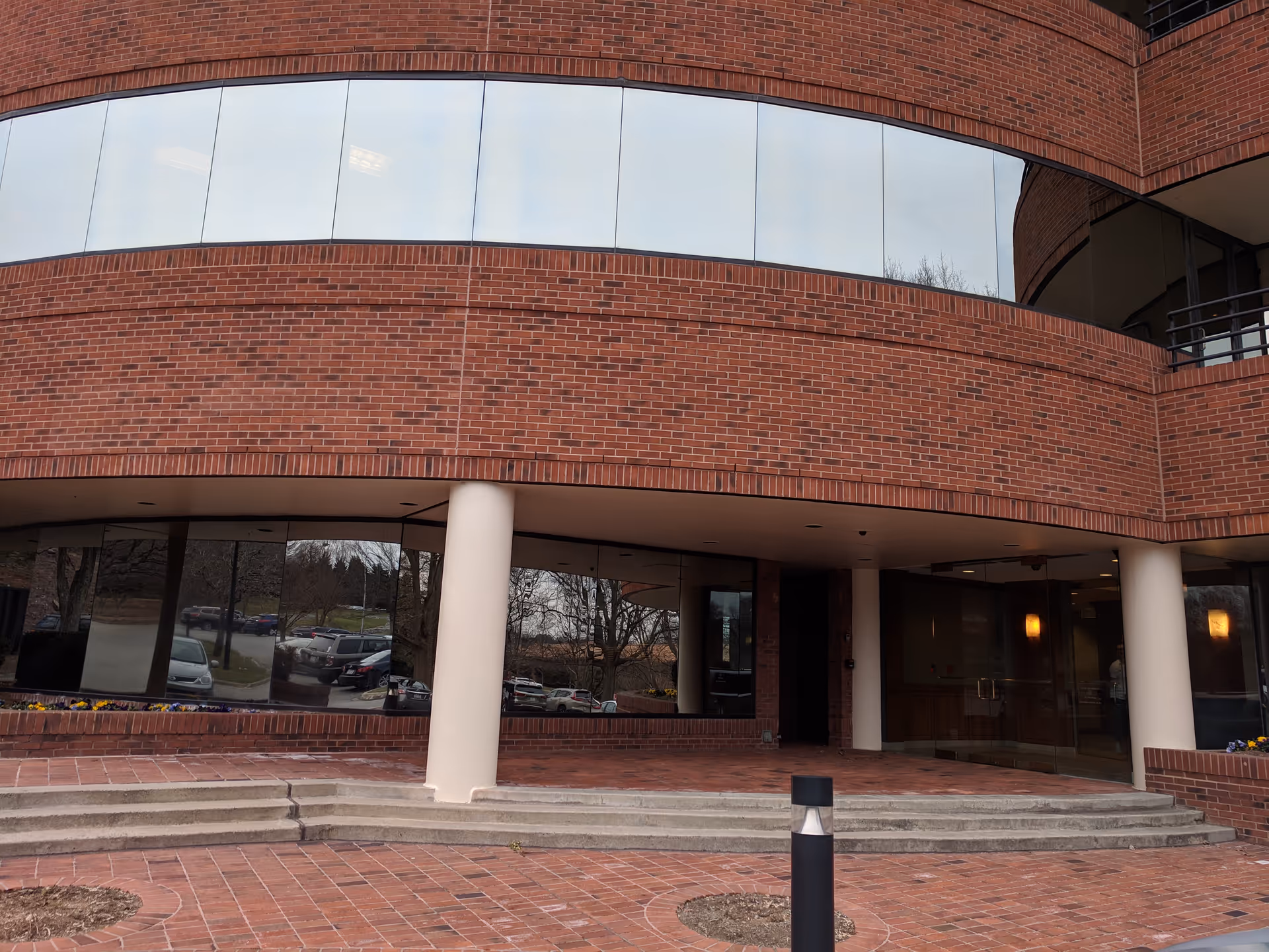 Brick building exterior with curved glass windows, front entrance, and white columns.