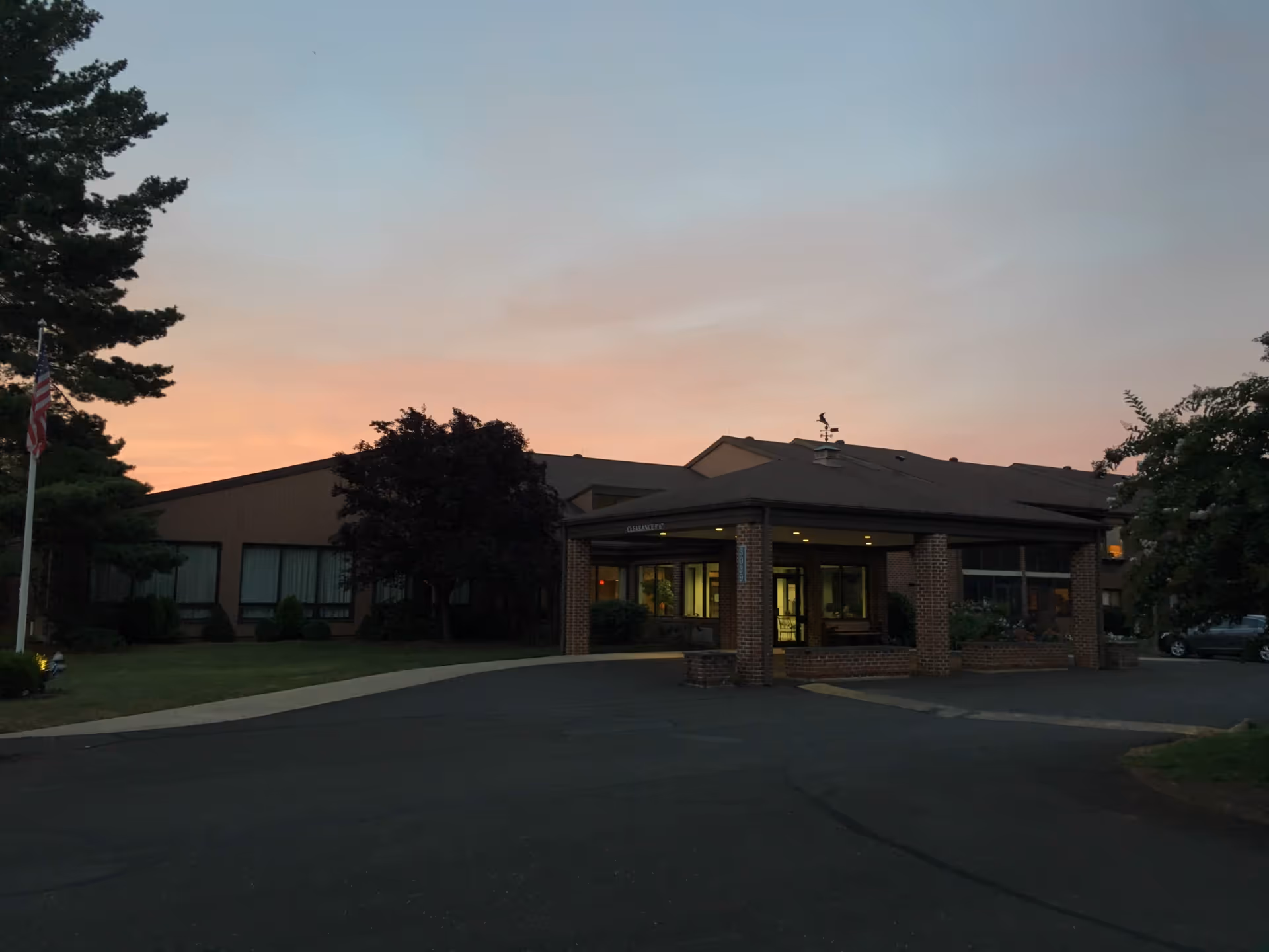 Sunset hues illuminate Cairnwood Village's brick entrance and driveway with trees.