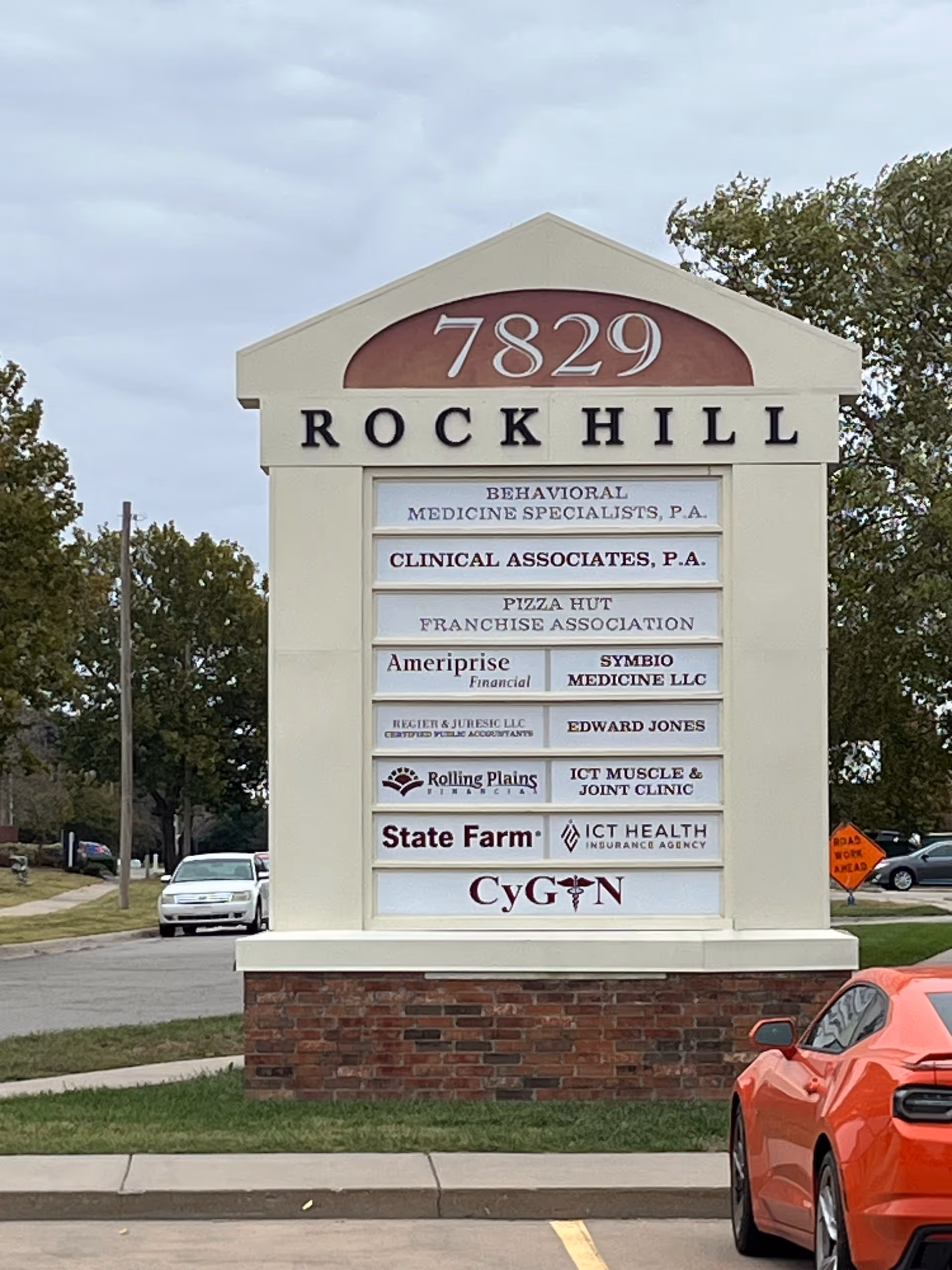 Tall stone sign with ROCKHILL and multiple tenant listings beside a parking lot.