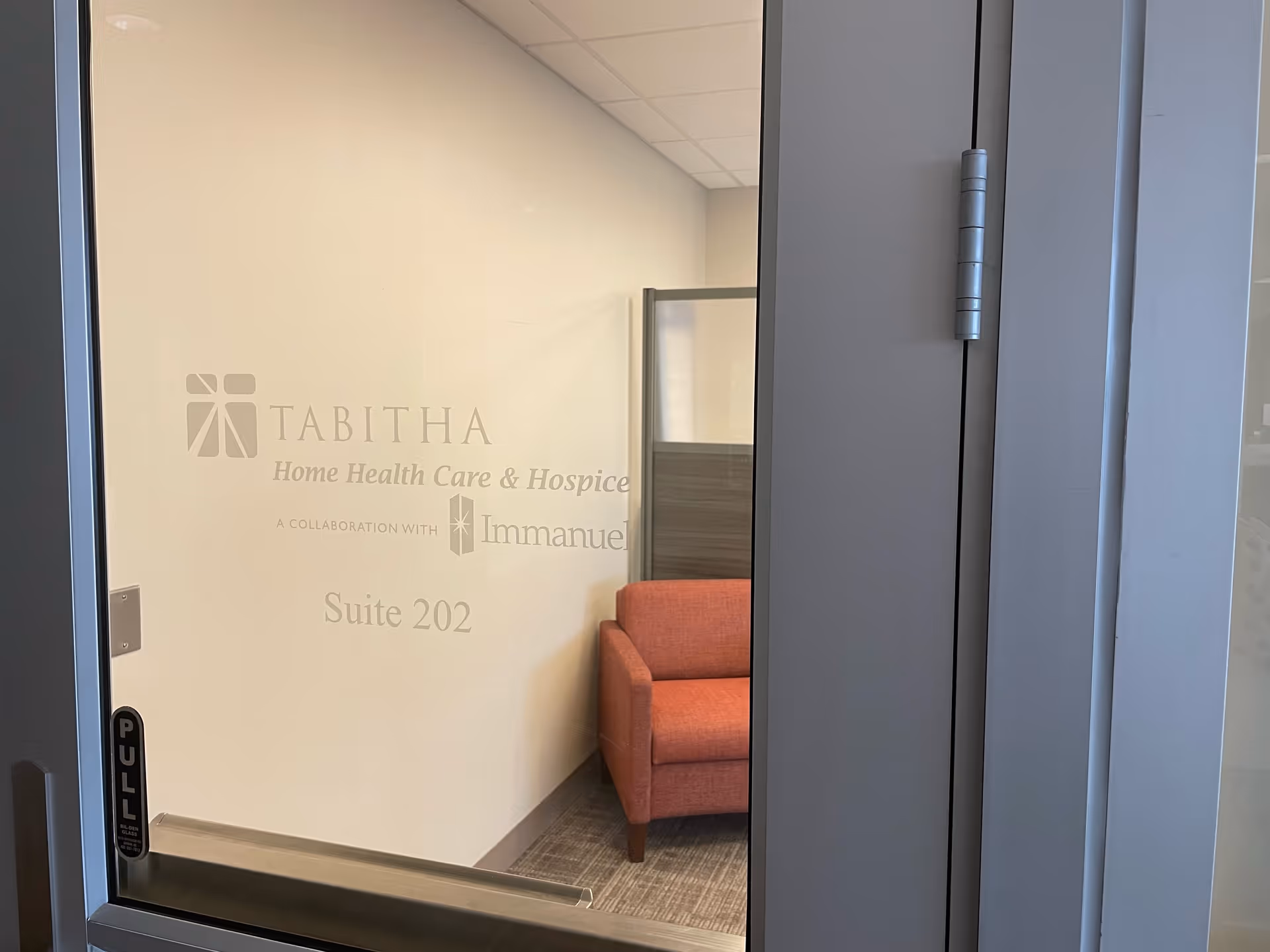 Glass door reveals Tabitha Home Health Care and Hospice suite with an orange waiting chair.