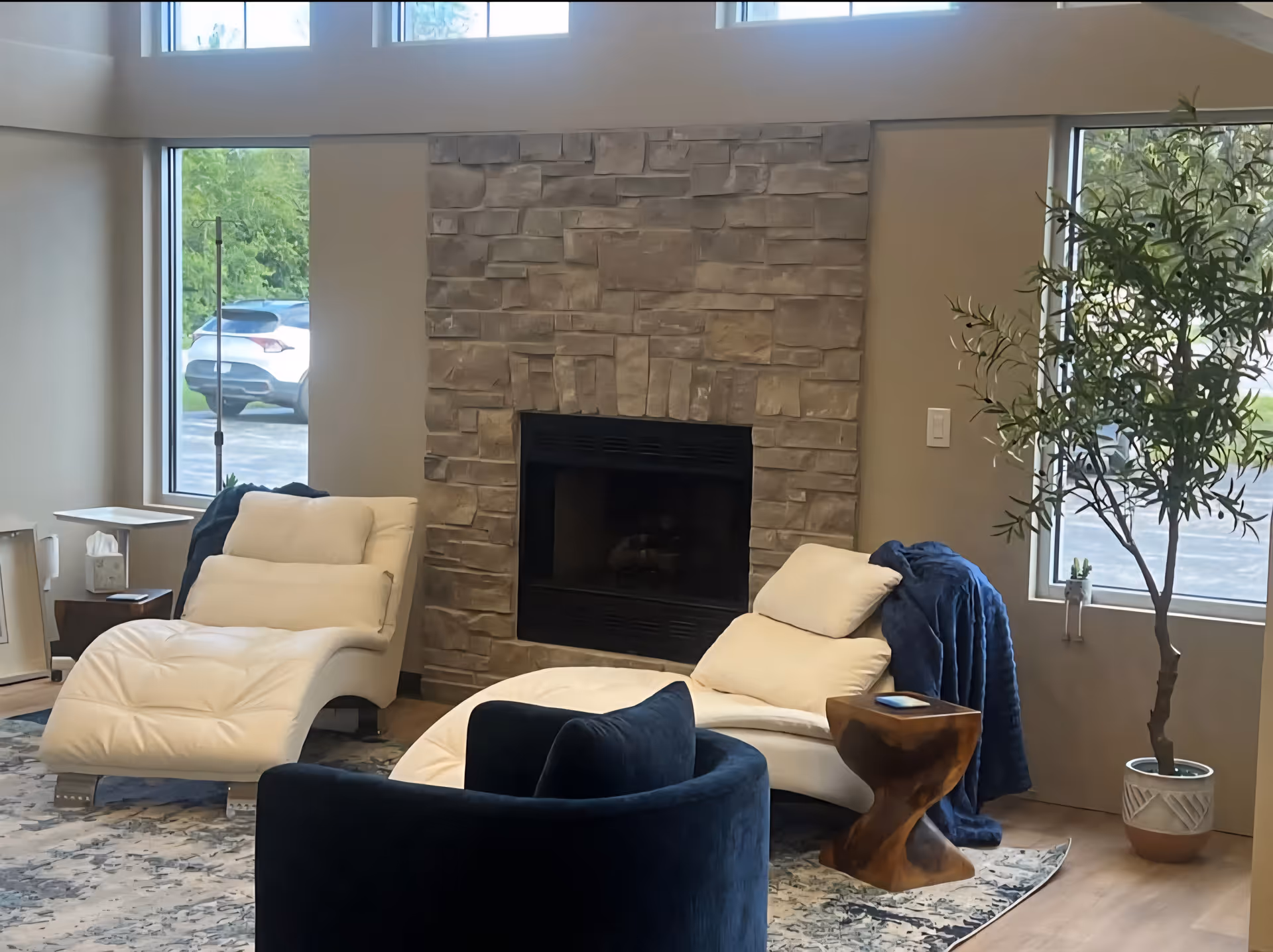 Modern living room in a senior facility with a stone fireplace and white lounge chairs.