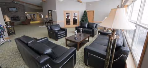 Spacious lounge with black leather sofas, coffee table, lamps, and a small Christmas tree.