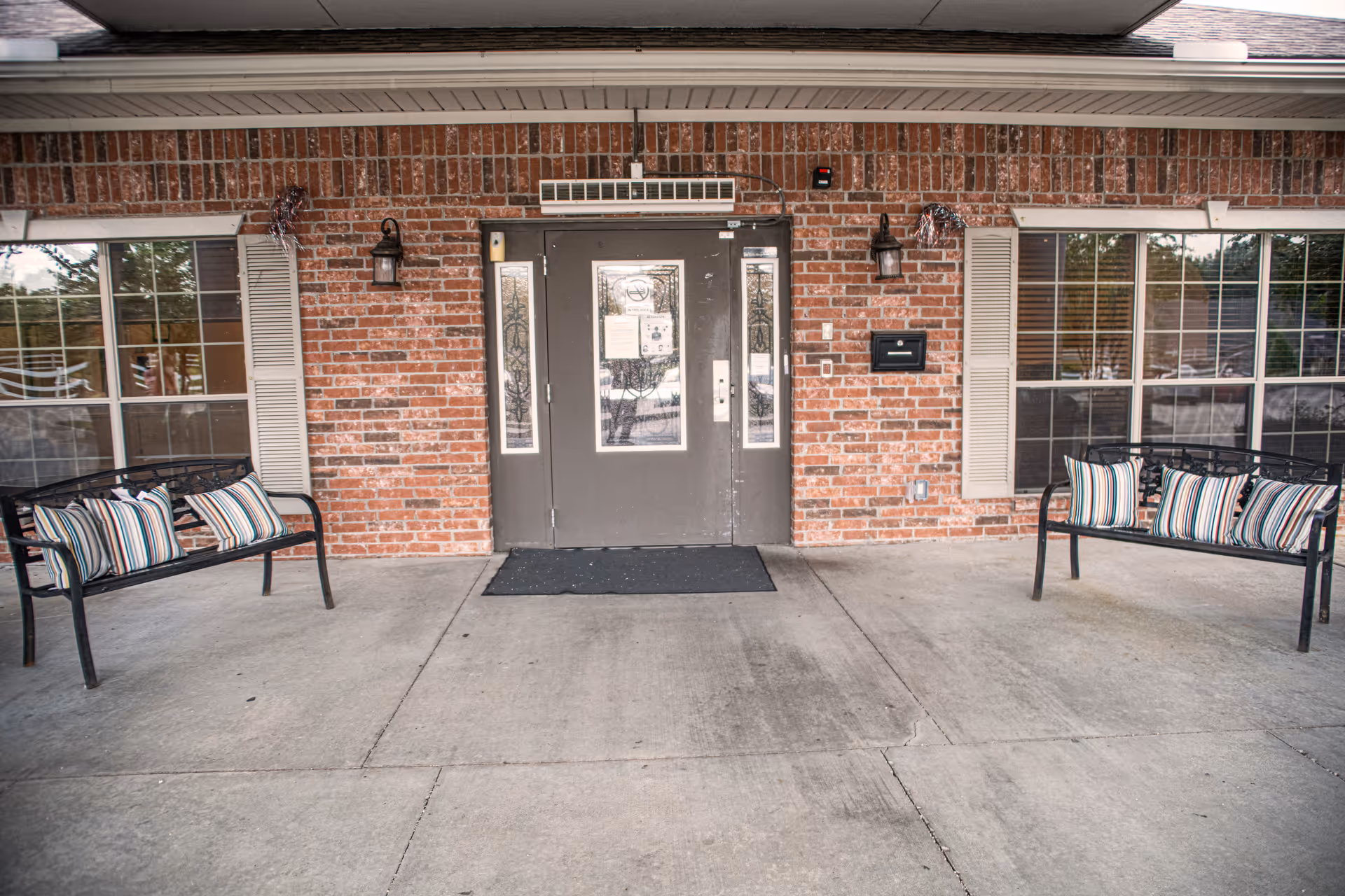 Brick exterior entrance with double doors and striped-cushion benches on both sides.