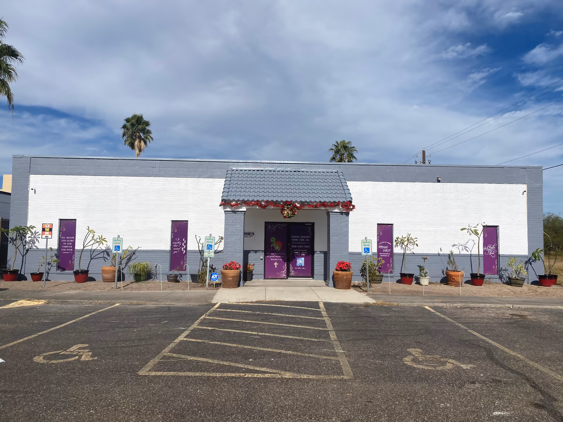 White-gray facility building with purple banners, decorative garland, and potted plants along the entrance.