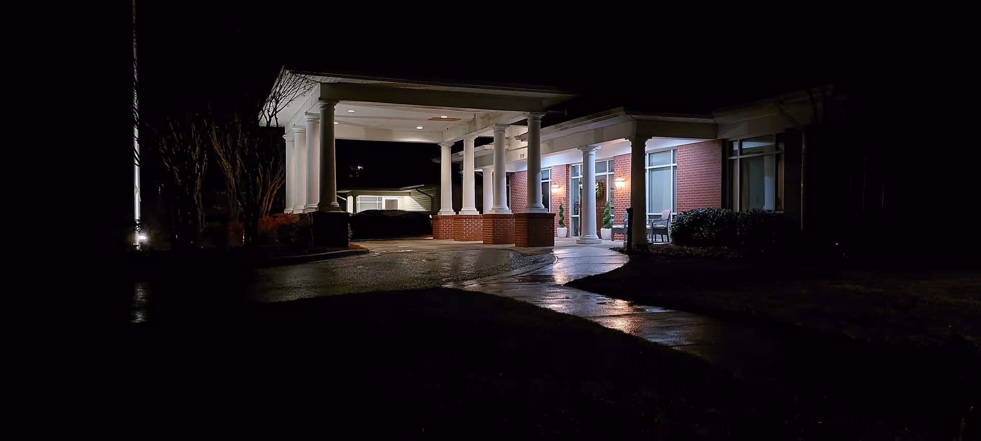 Night exterior view of a senior living facility entrance with a covered portico and columns.