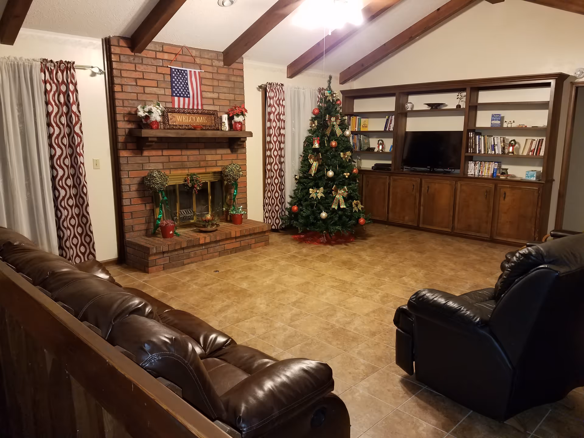 Cozy living room with brick fireplace, Christmas tree, leather seating, and built-in shelves.