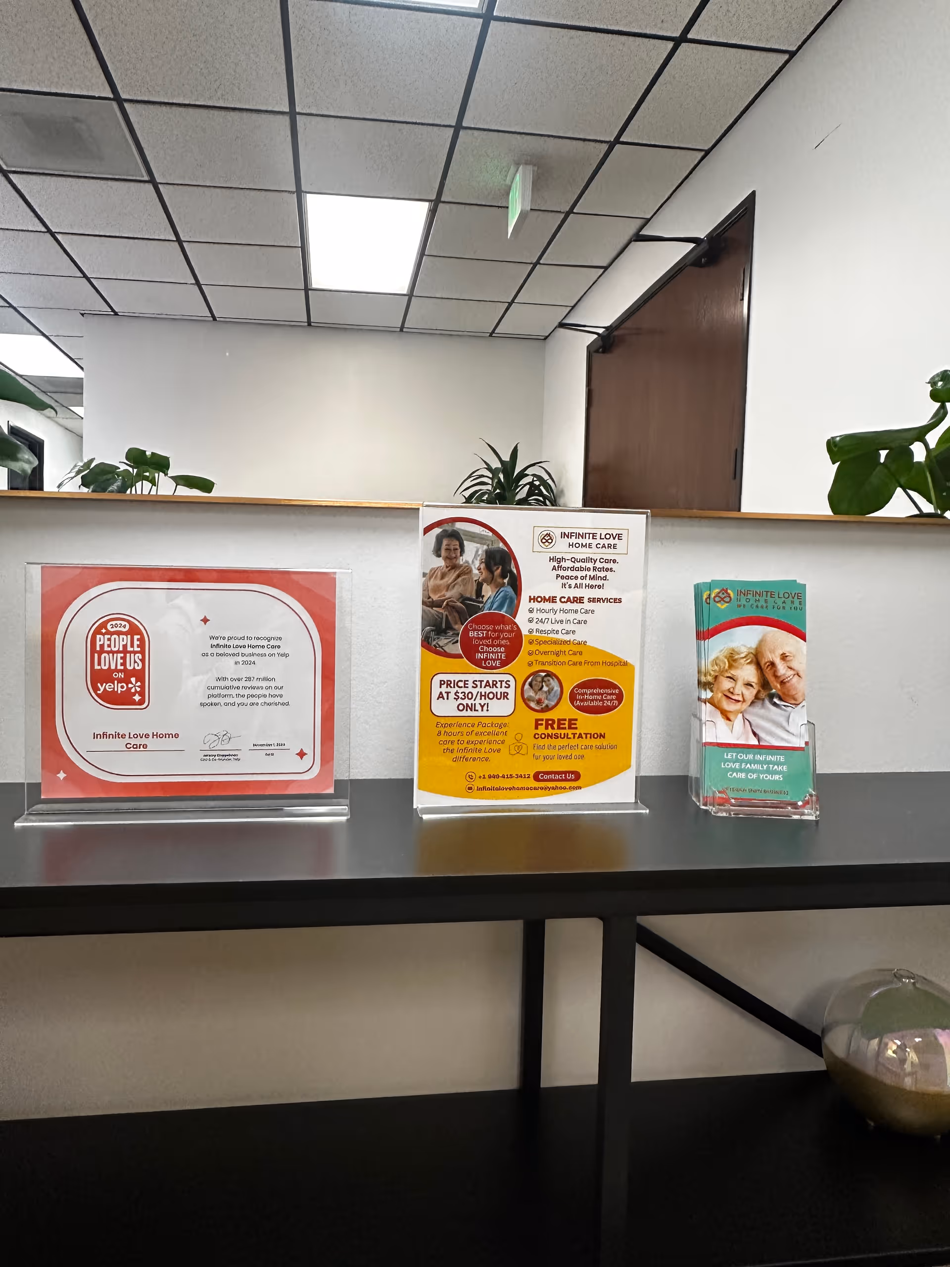 A reception counter with brochures, potted plants, and a doorway in a quiet lobby.
