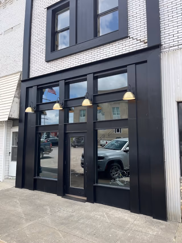 Black-framed storefront with tall glass windows and doors on a brick exterior.