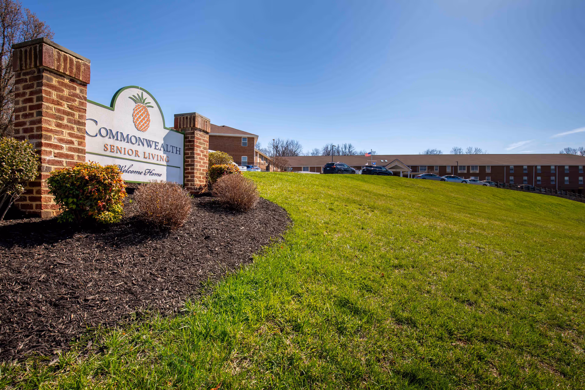 Front exterior view of Commonwealth Senior Living at Front Royal with sign and hillside lawn.