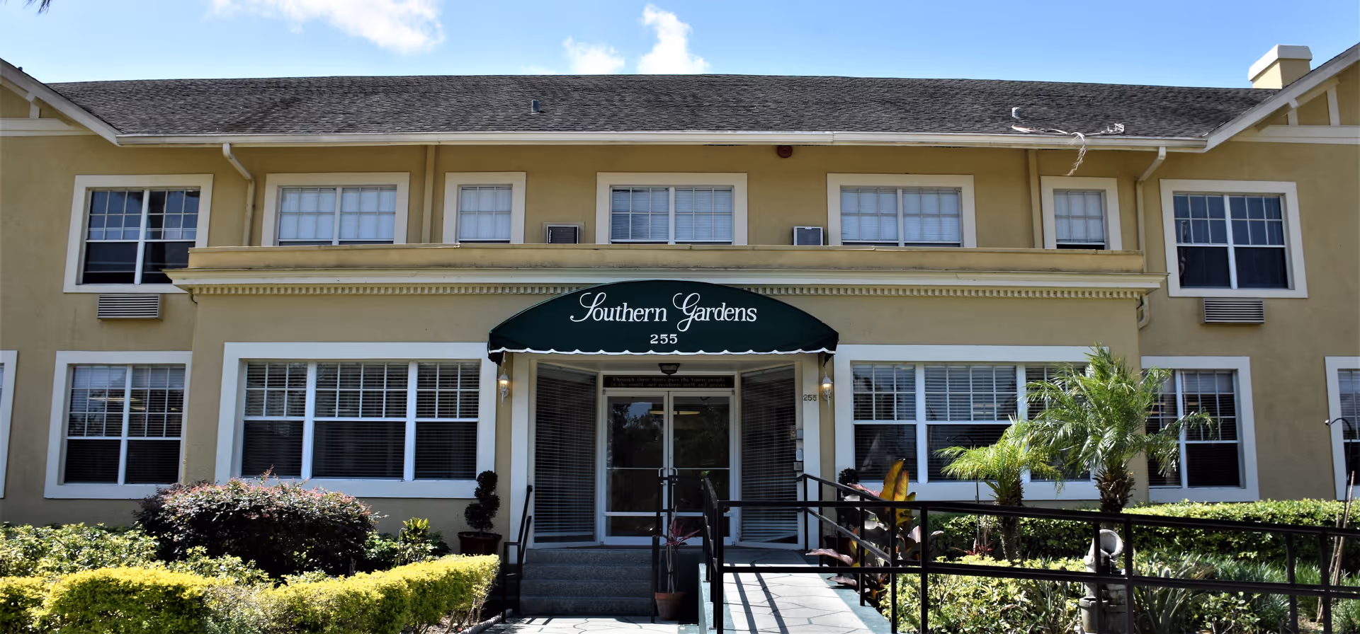 Front view of a yellow senior living building with a green awning over the entrance.