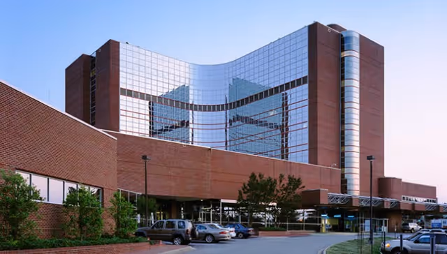 Exterior view of a modern brick-and-glass hospital-style building with a parking area.