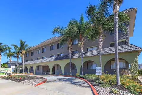 Two-story Pacific Pointe senior living building with palm trees and arched entryways.