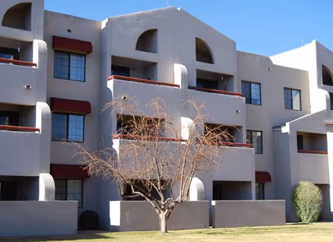 Exterior view of a multi-story senior living building with balconies and a bare tree.
