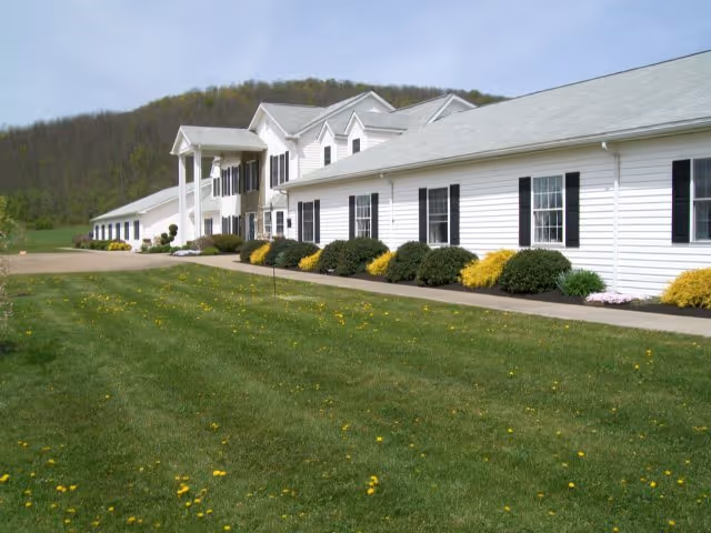 A single-story white senior living facility exterior with a manicured lawn.