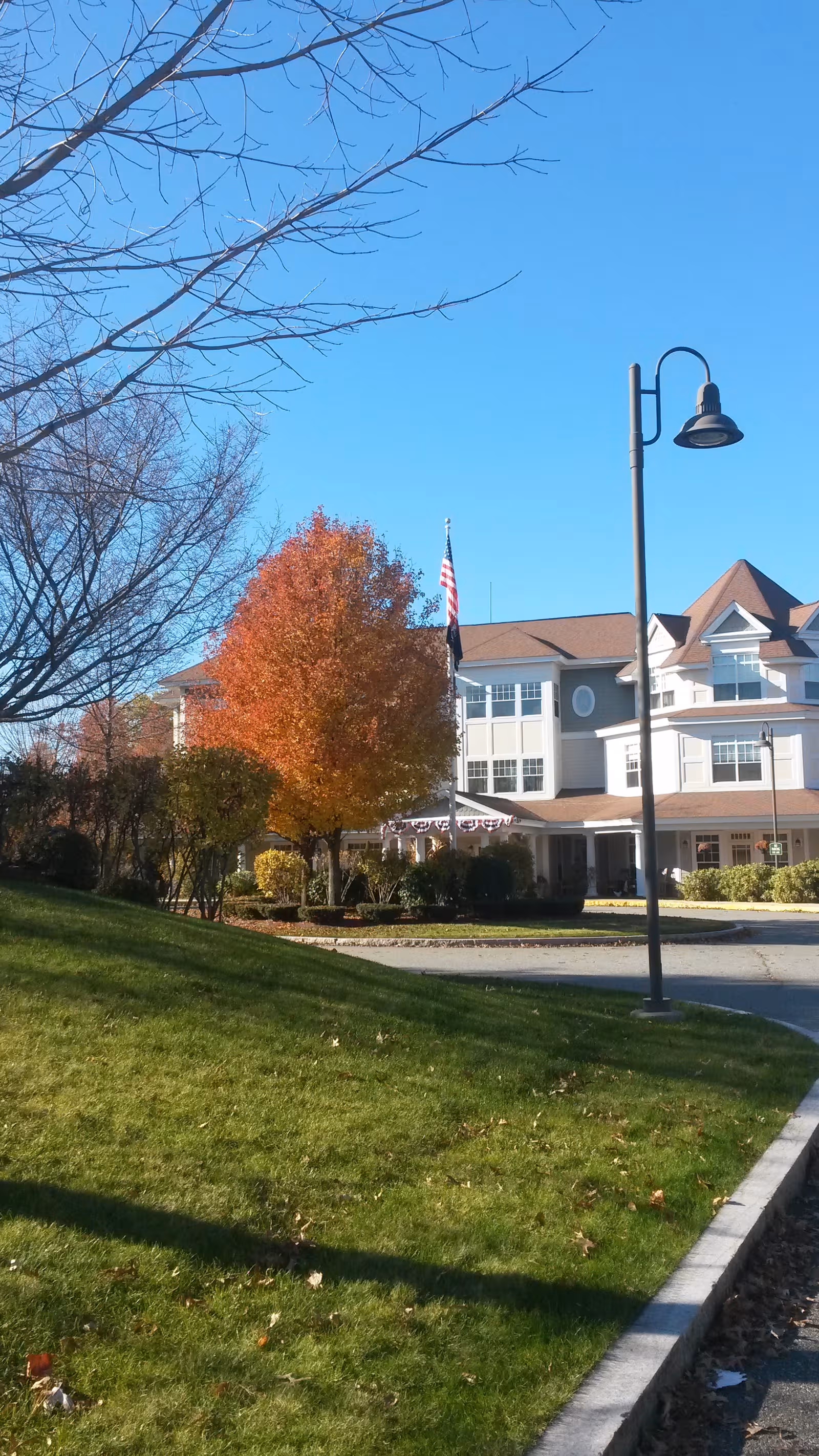 Tamarisk Senior Living exterior building with flag, manicured lawn, trees, and a street lamp.