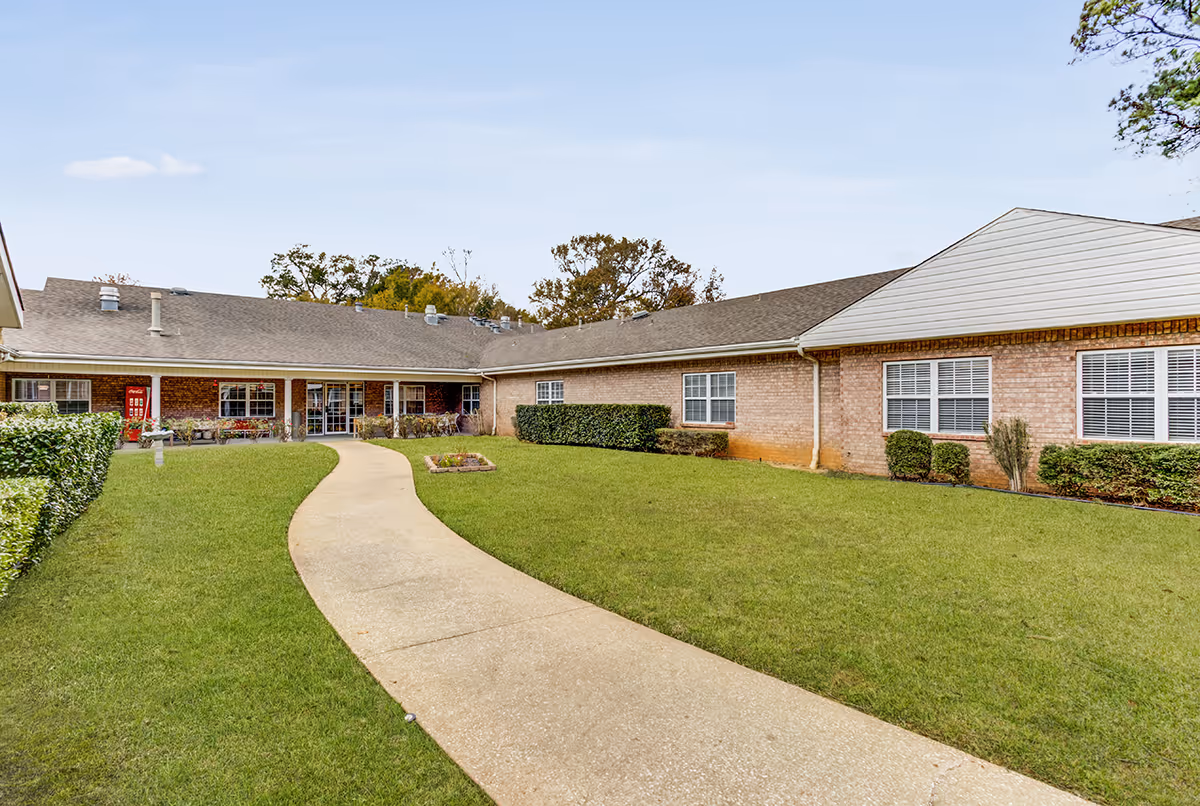 Brick senior living building with a curved concrete walkway and well-kept lawn.