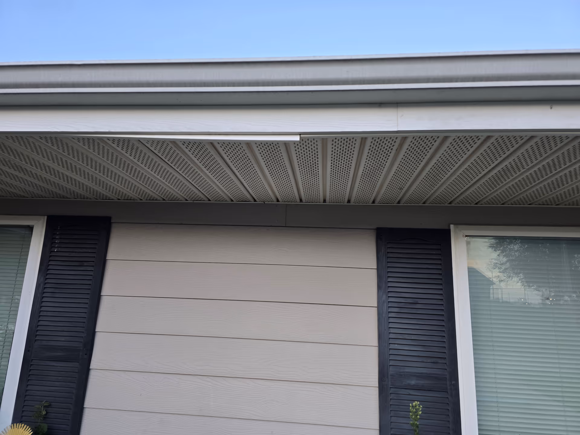 Close-up of a beige siding building exterior with shutters and a vented overhang.