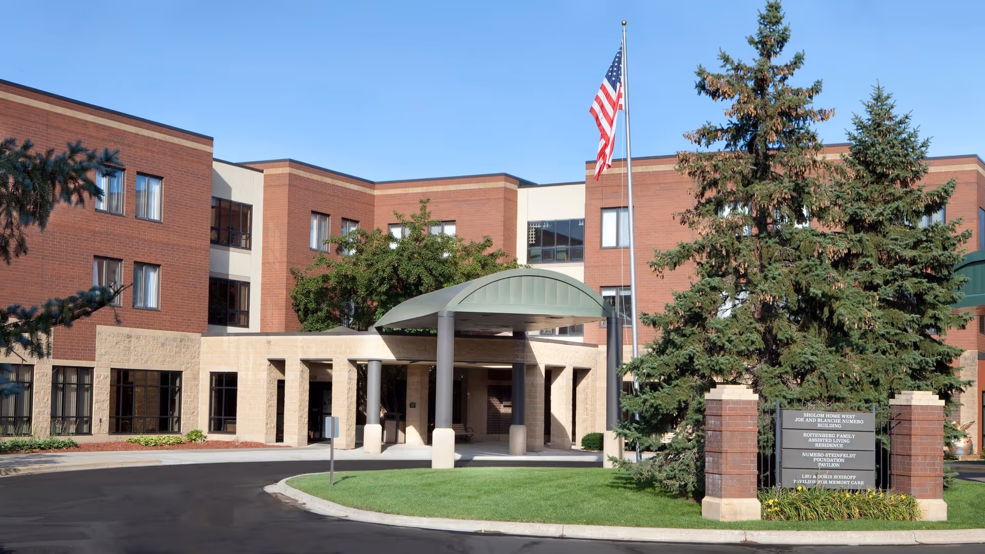 Exterior view of a brick senior living building with entrance canopy and flagpole.