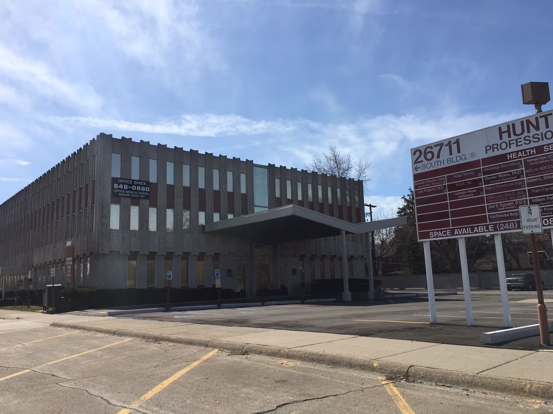 Exterior view of a concrete office building with curved entrance canopy and parking lot.