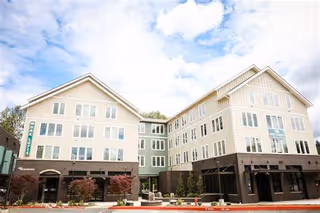 Two-story beige senior living building with brick base and storefront entrances along a street.