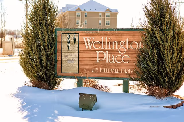 Snow-covered Wellington Place sign in front of a multi-story building.