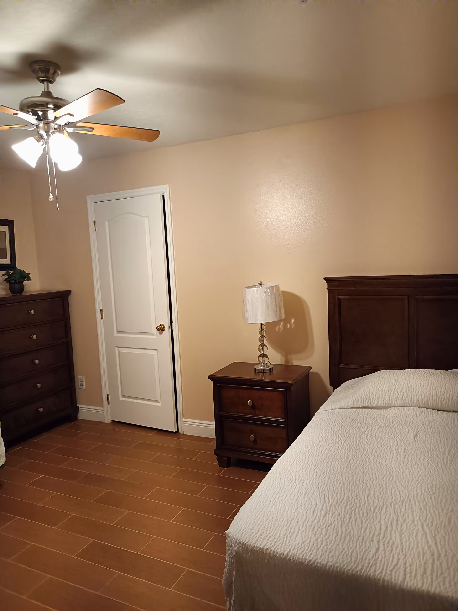 Bedroom with dark wood furniture, bed, nightstand lamp, dresser, and ceiling fan.