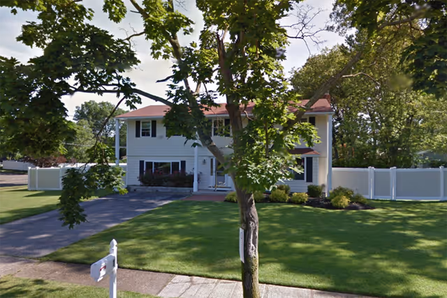 Exterior view of Sylvie's Cove: a two-story house with a green lawn, driveway, and trees.