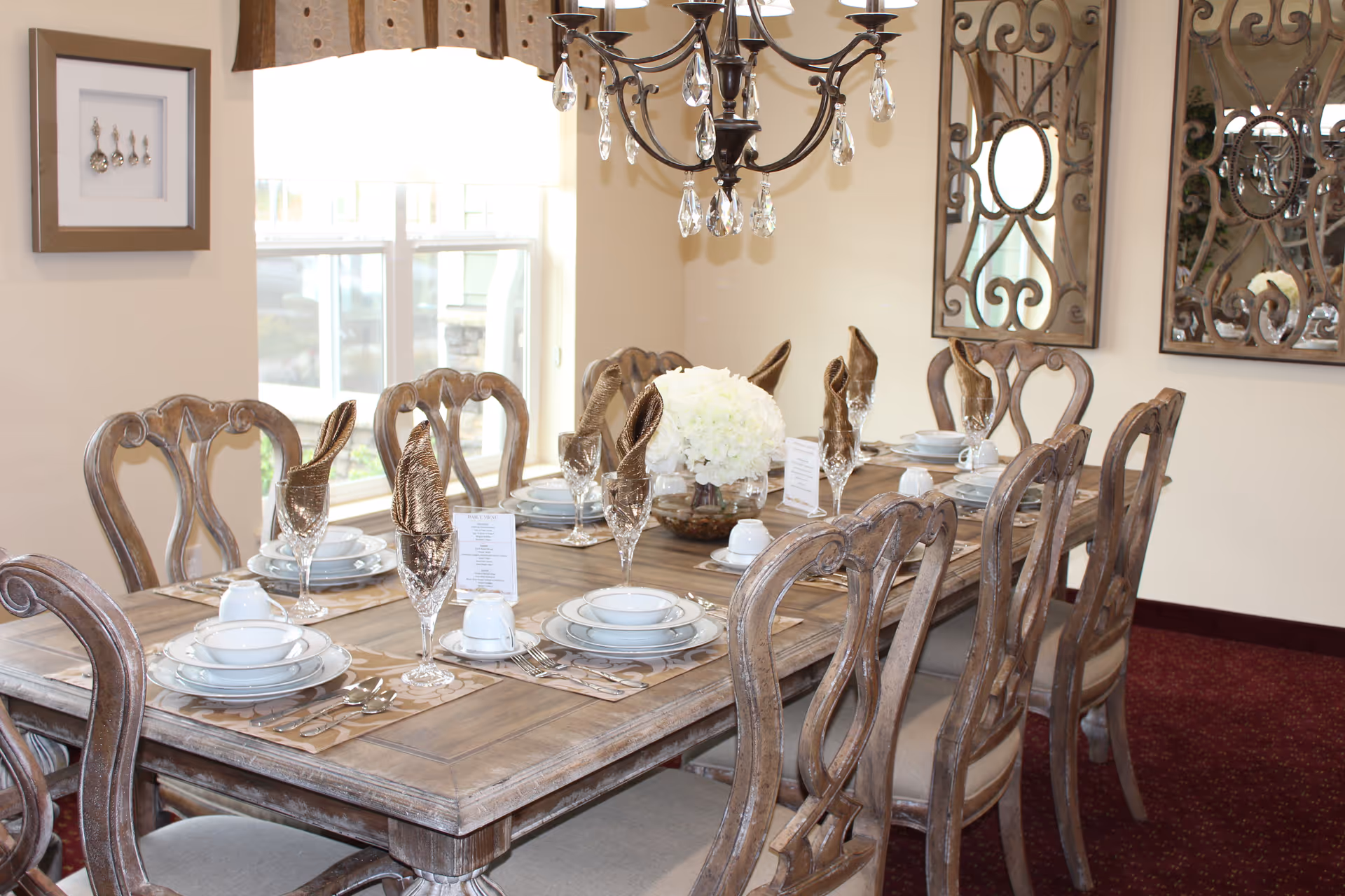 Long wooden dining table set for a formal meal, with crystal chandeliers overhead.