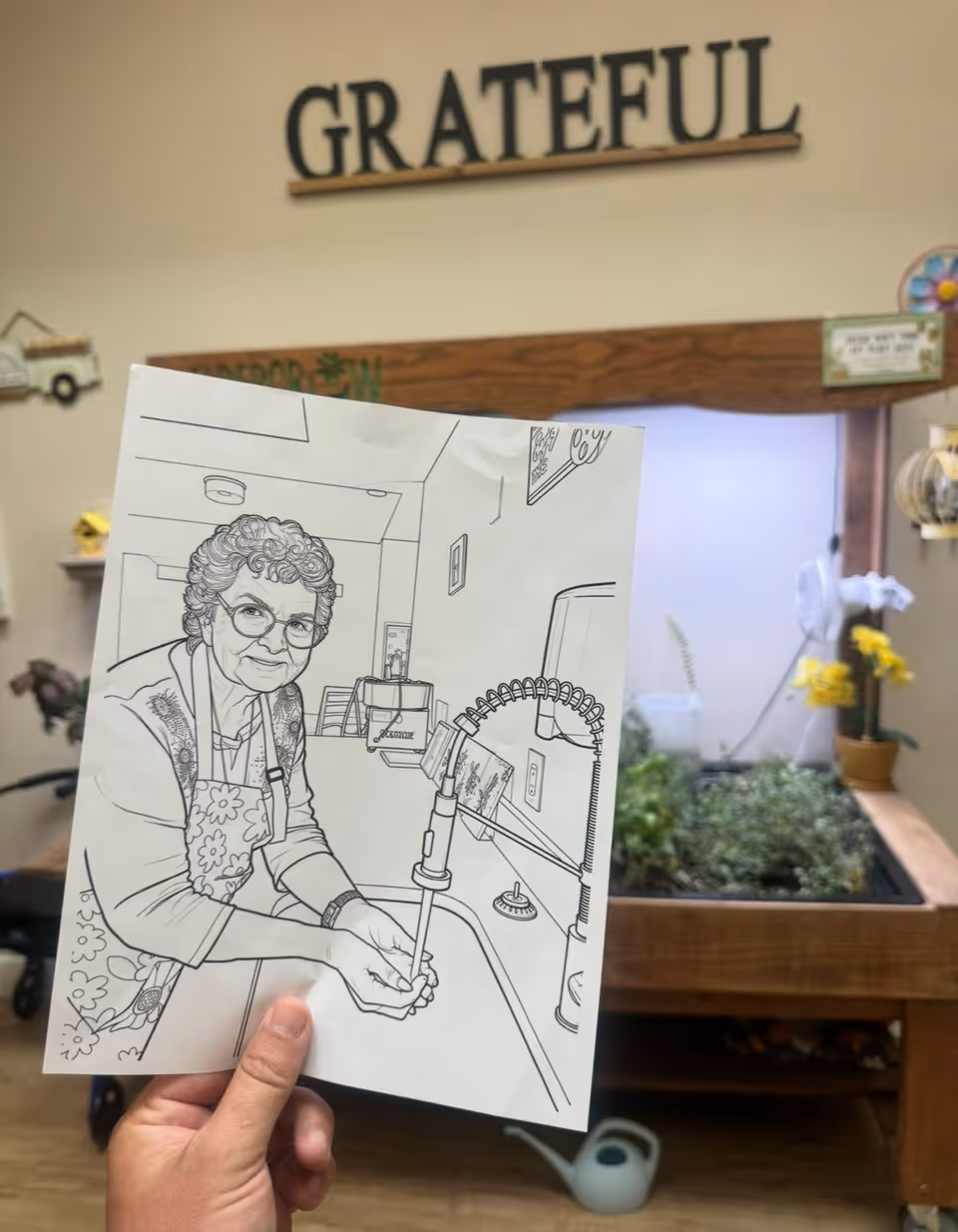 A hand holds a line-drawing sheet inside Mosaic Gardens at Scottsdale, with a sink in background.