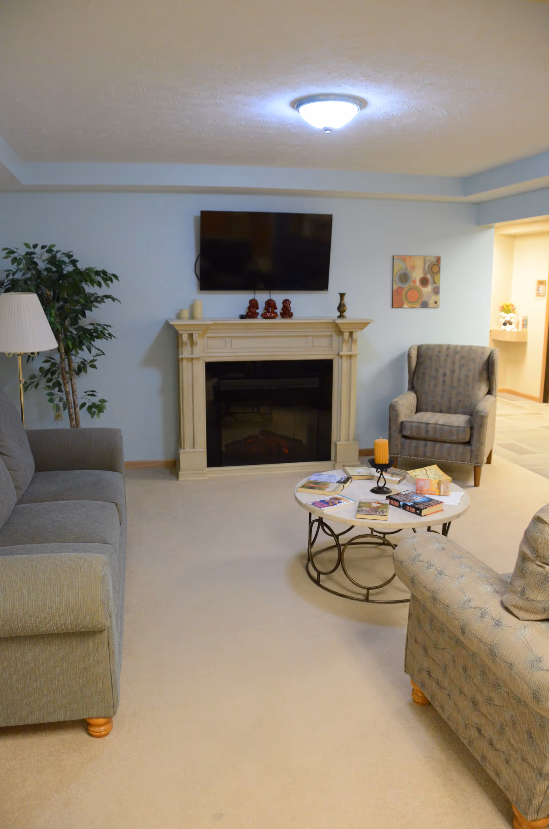 Cozy living room lounge with sofa, armchairs, fireplace, mounted TV, and magazines on a coffee table.