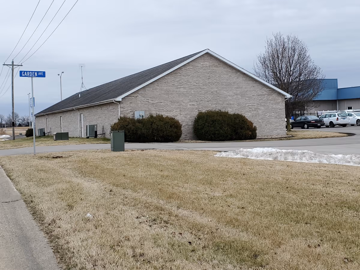 Exterior view of a brick, single-story building with a grassy lawn and parking lot.