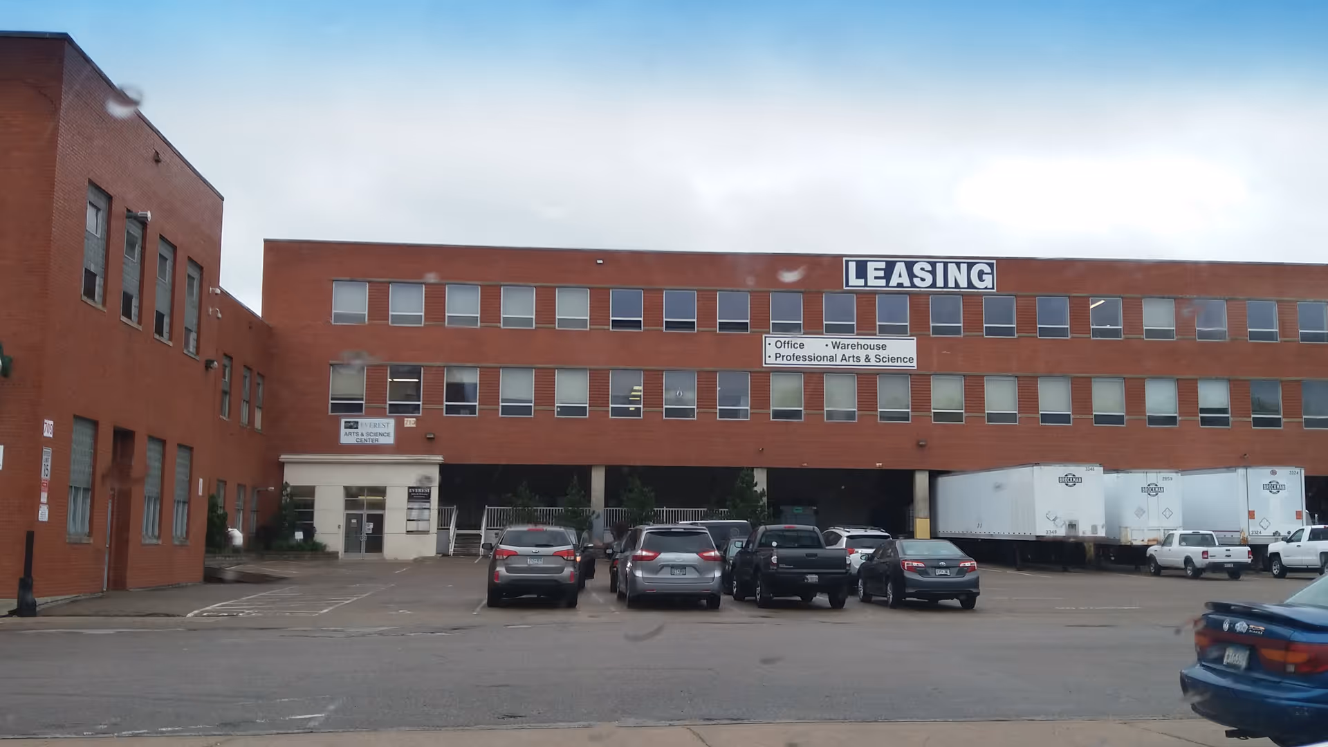 Brick office building with a prominent LEASING sign and a parking lot in front.