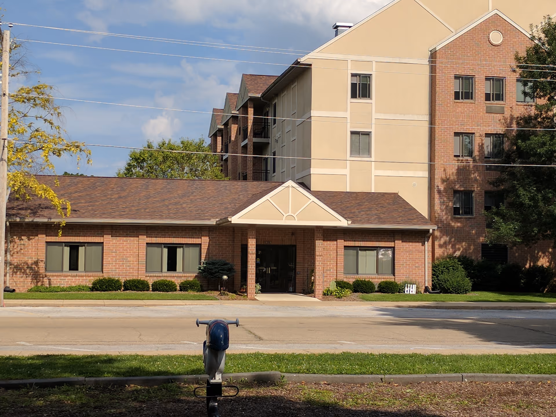 Brick and tan multi-story building with a central entrance and manicured landscaping along the street.