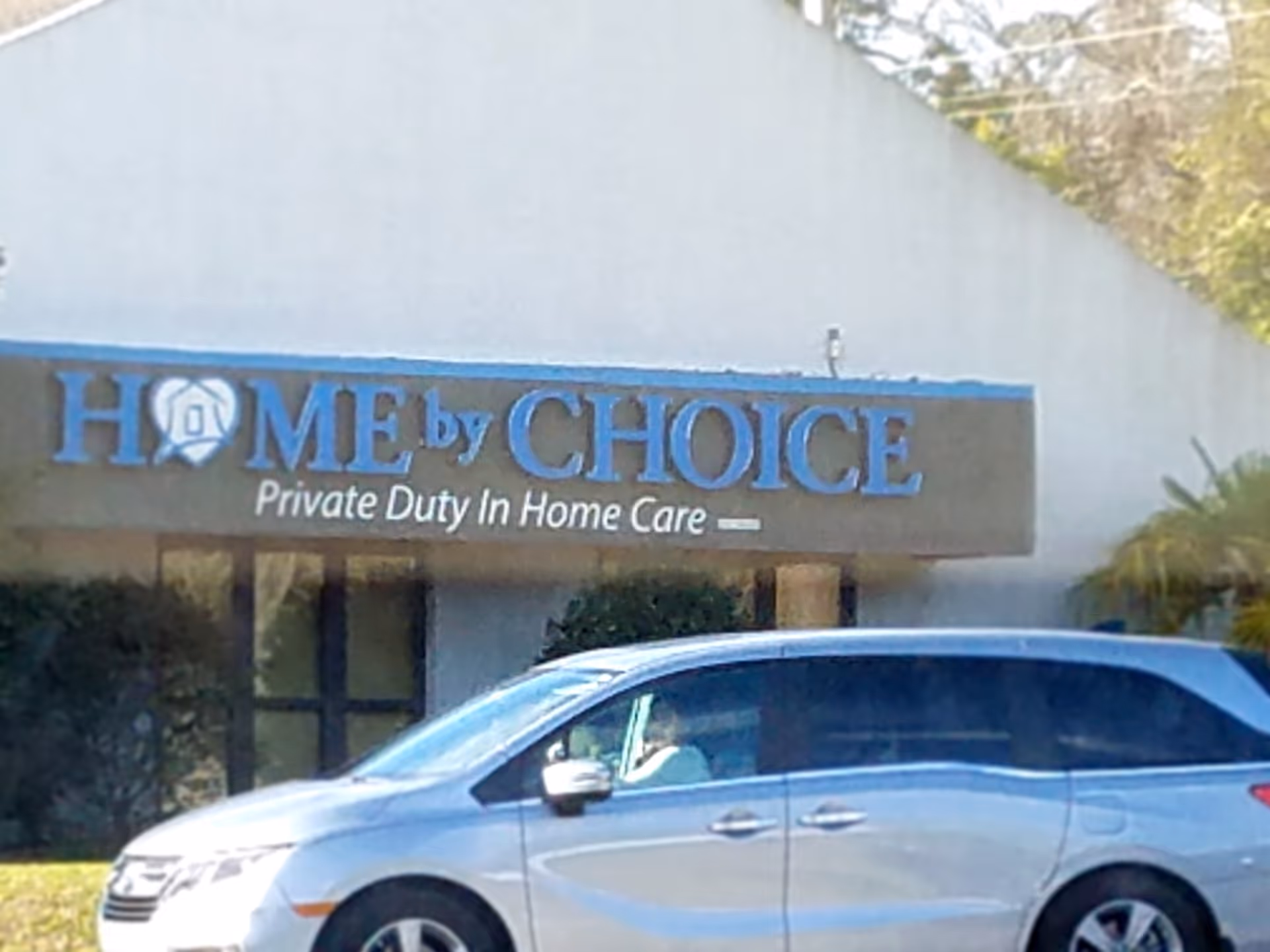 Exterior of a facility with a blue Home by Choice sign and a car in front.
