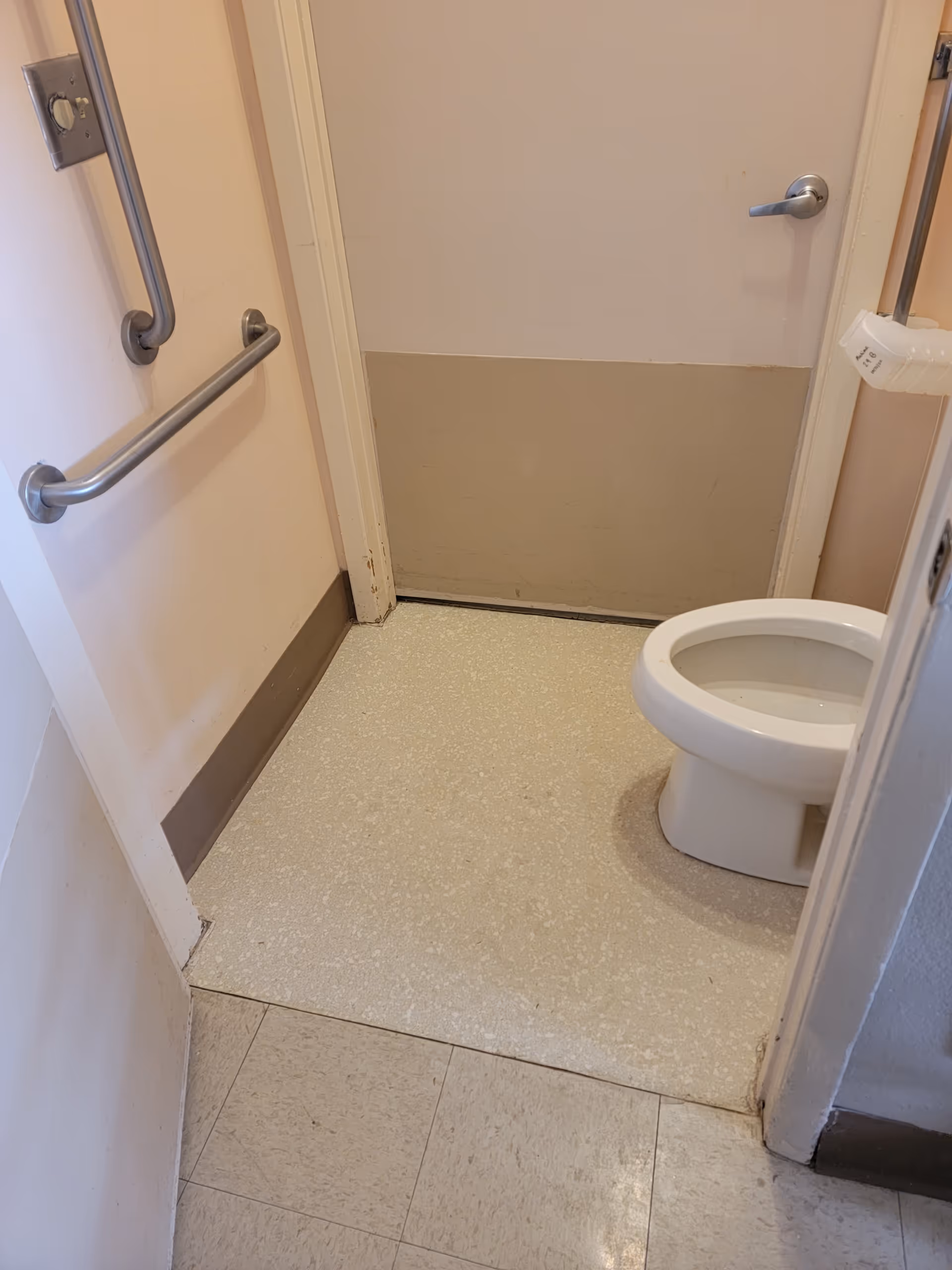 Small accessible bathroom with grab bars and a toilet in a senior living facility.