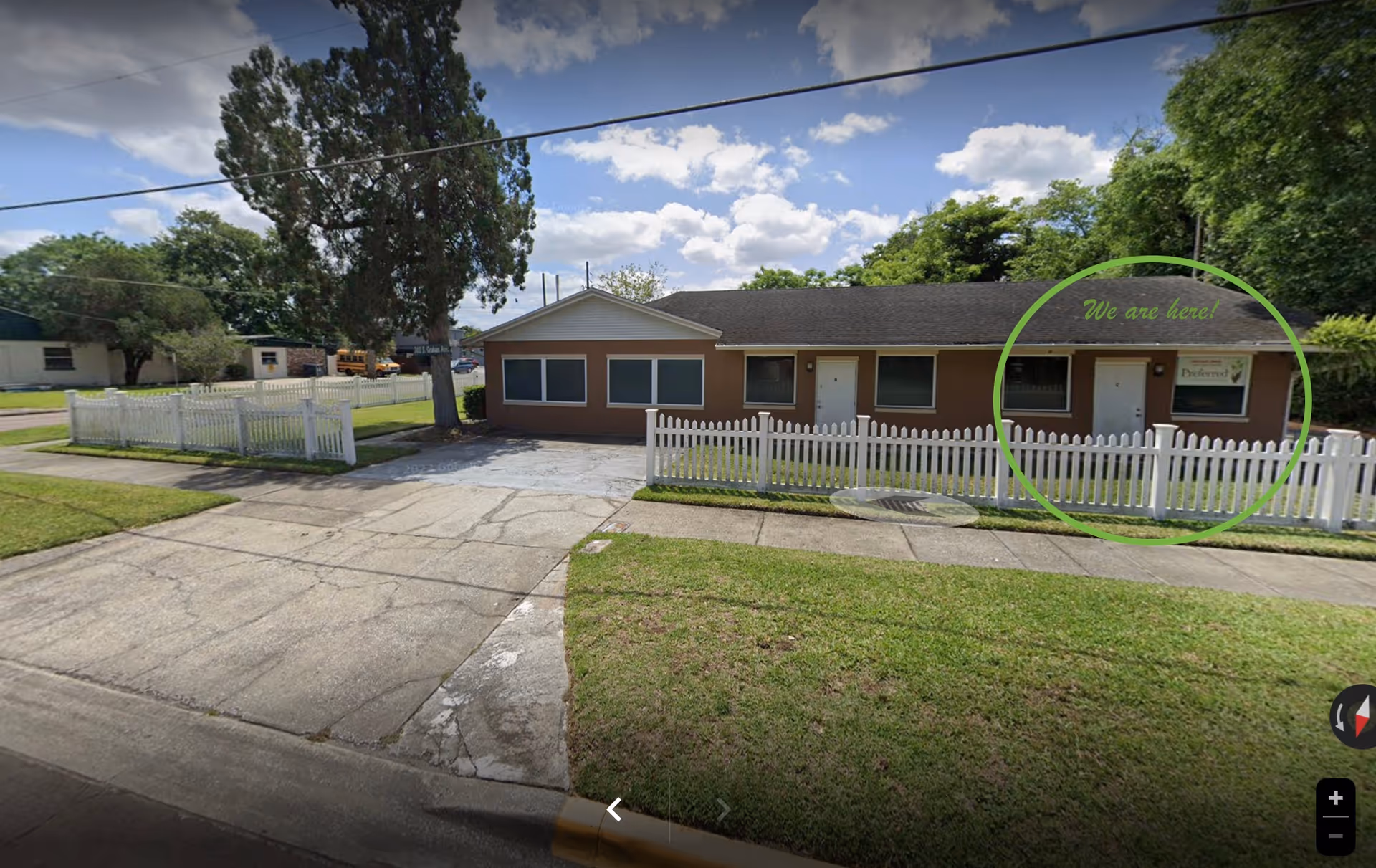 Single-story brown building with white picket fence and a sign at the entrance.